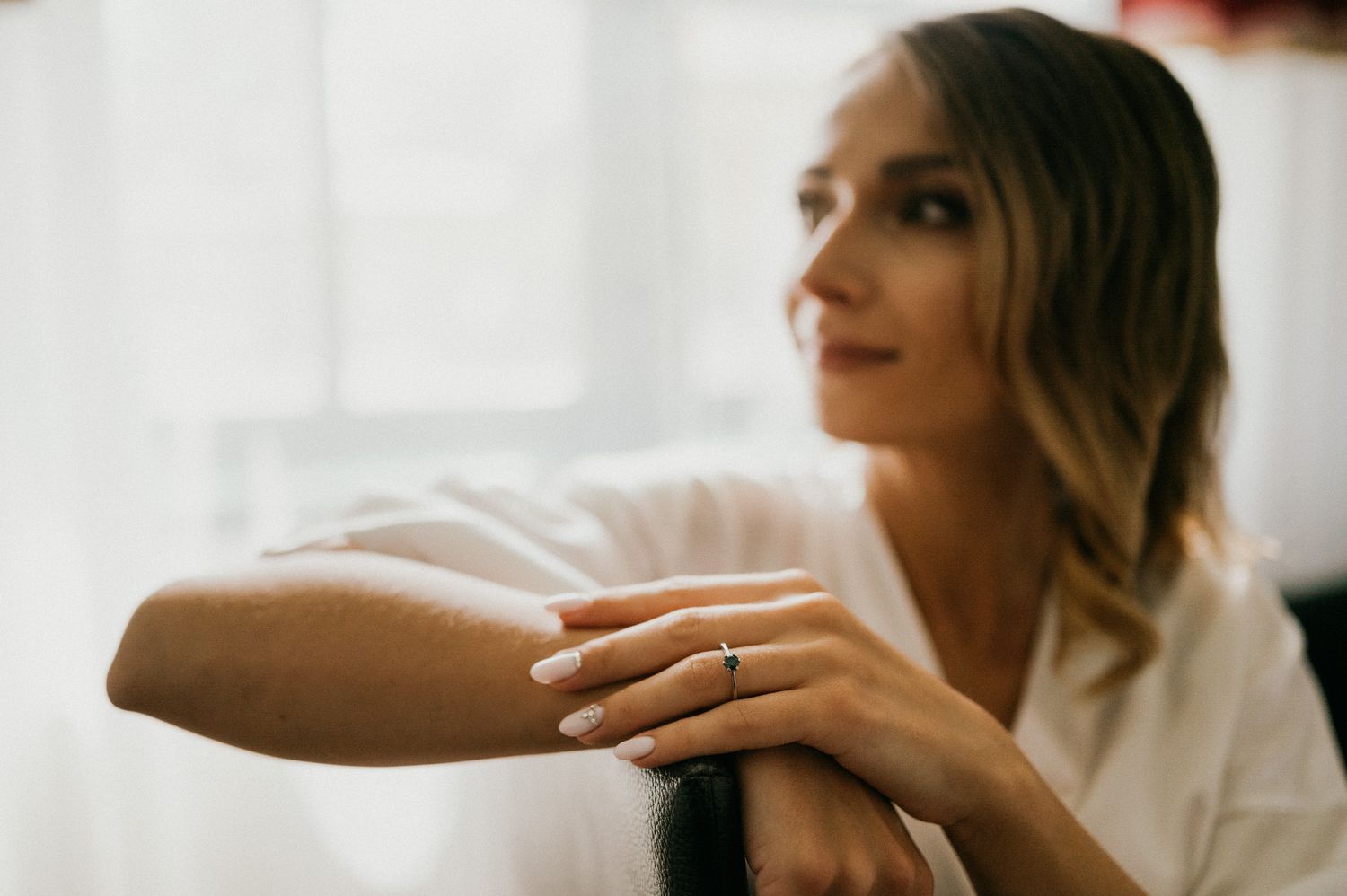 Side profile of person in white robe showing engagement ring in natural light.