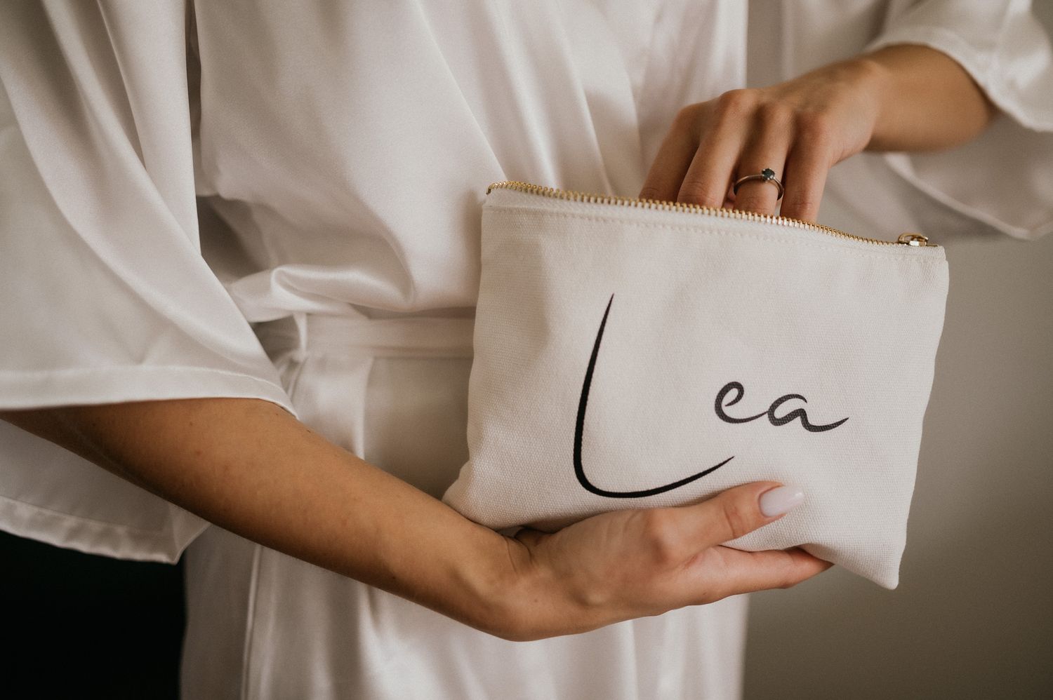 Hands holding a white leather clutch with 'Lea' text during wedding preparations.