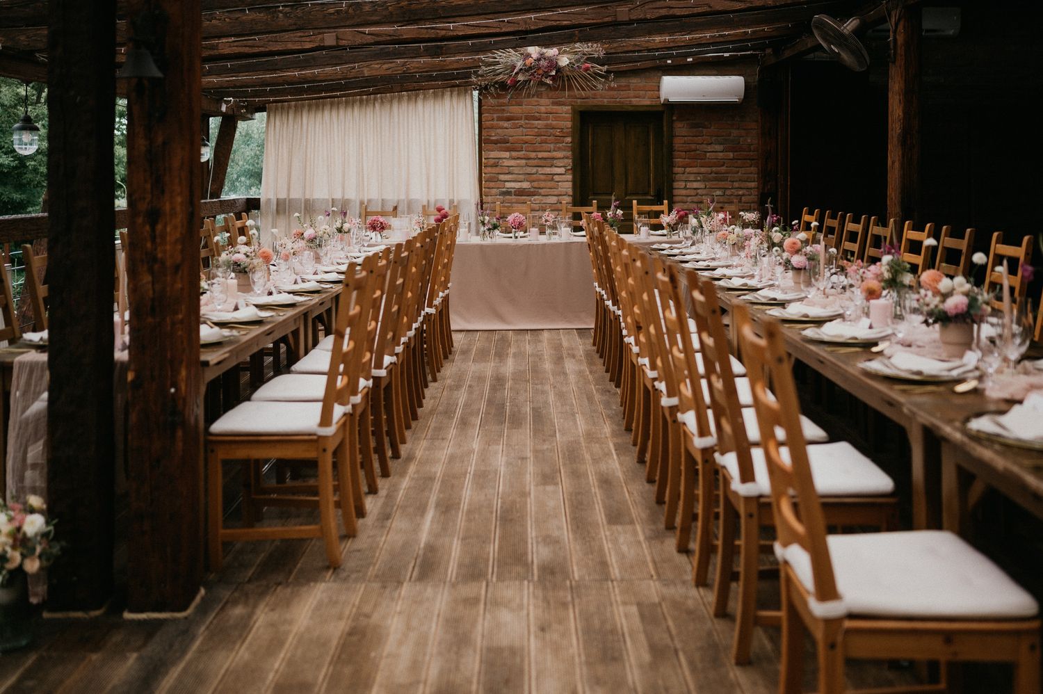 Long wooden tables arranged in rows at a rustic indoor wedding reception venue.