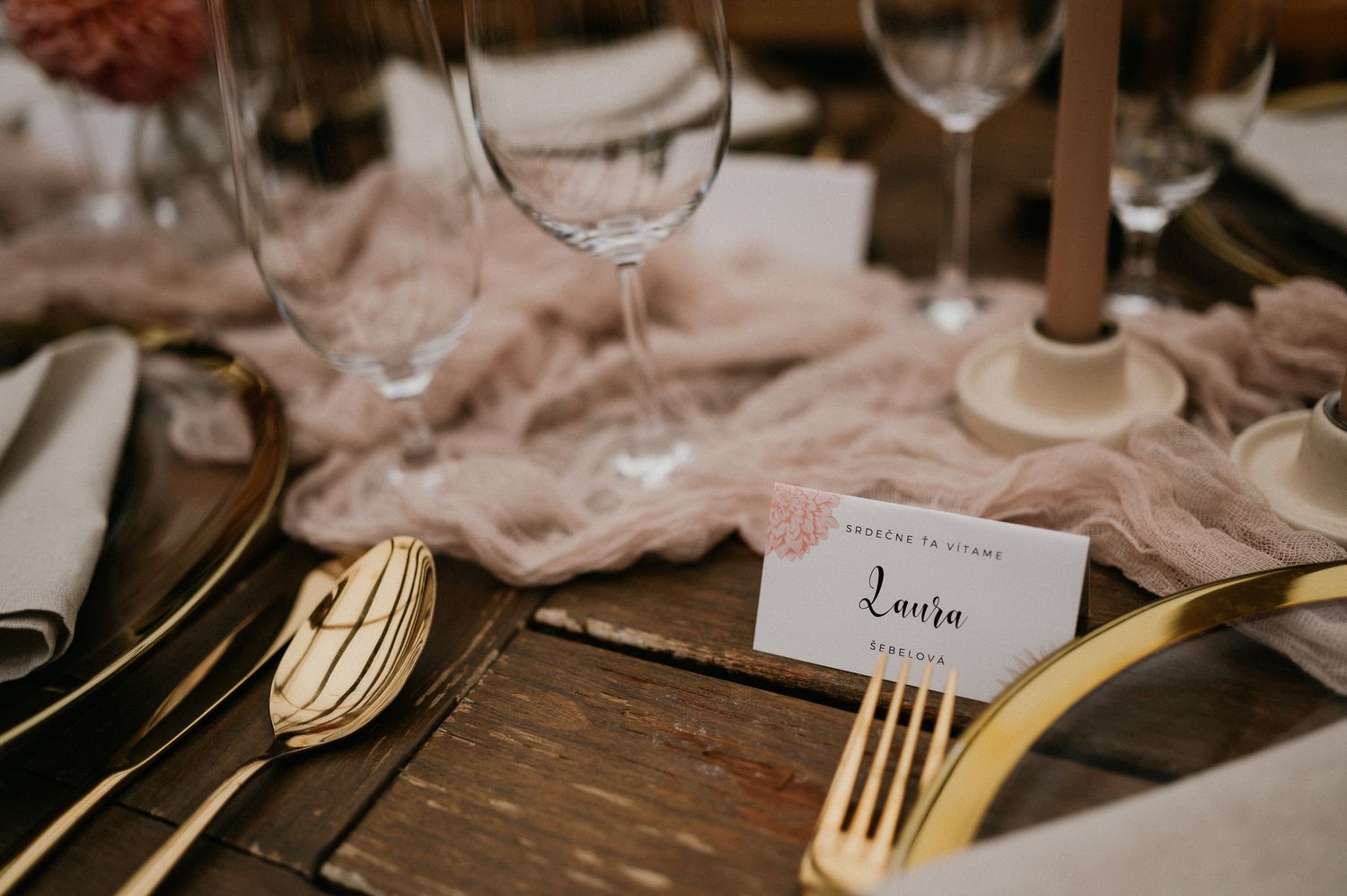 Place setting detail with gold cutlery and name card on a wooden table with blush accents.