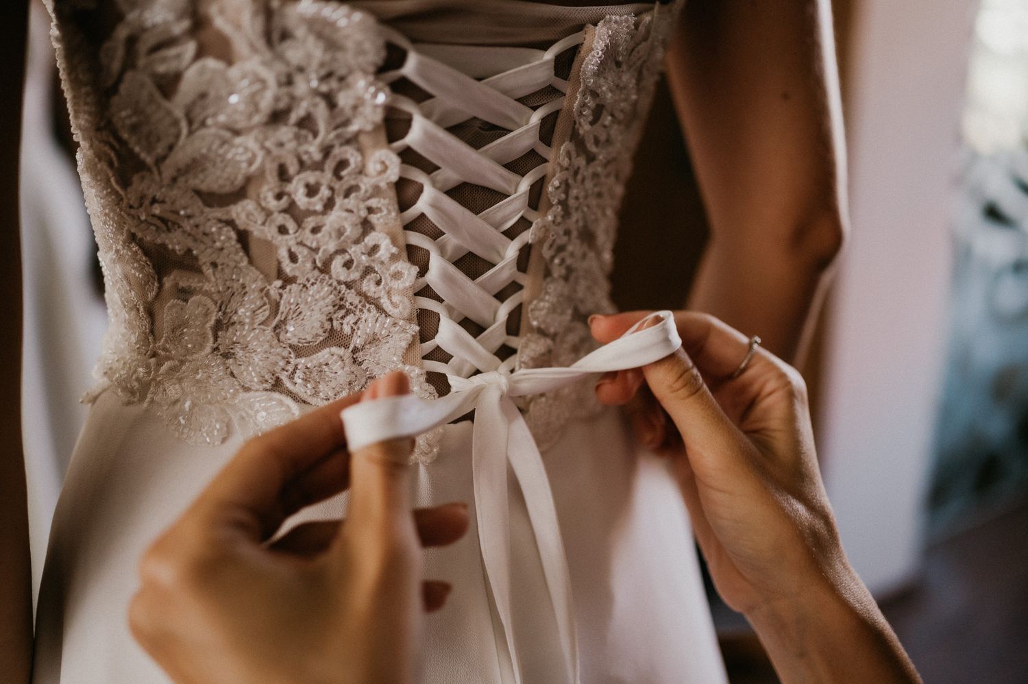 Detailed shot of intricate lace corset being laced up on wedding dress.