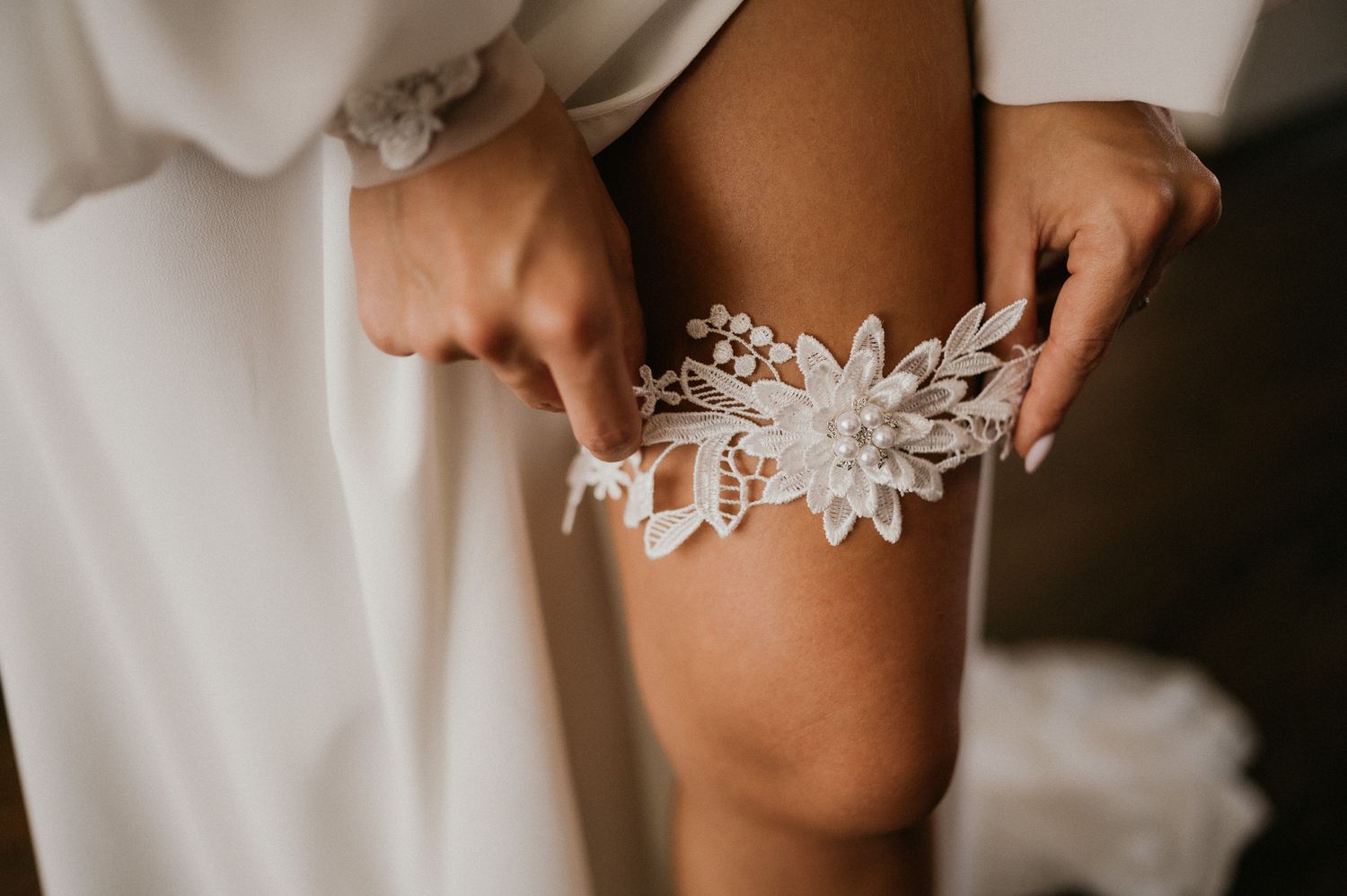 Close-up of delicate floral lace garter being held against white wedding dress fabric.
