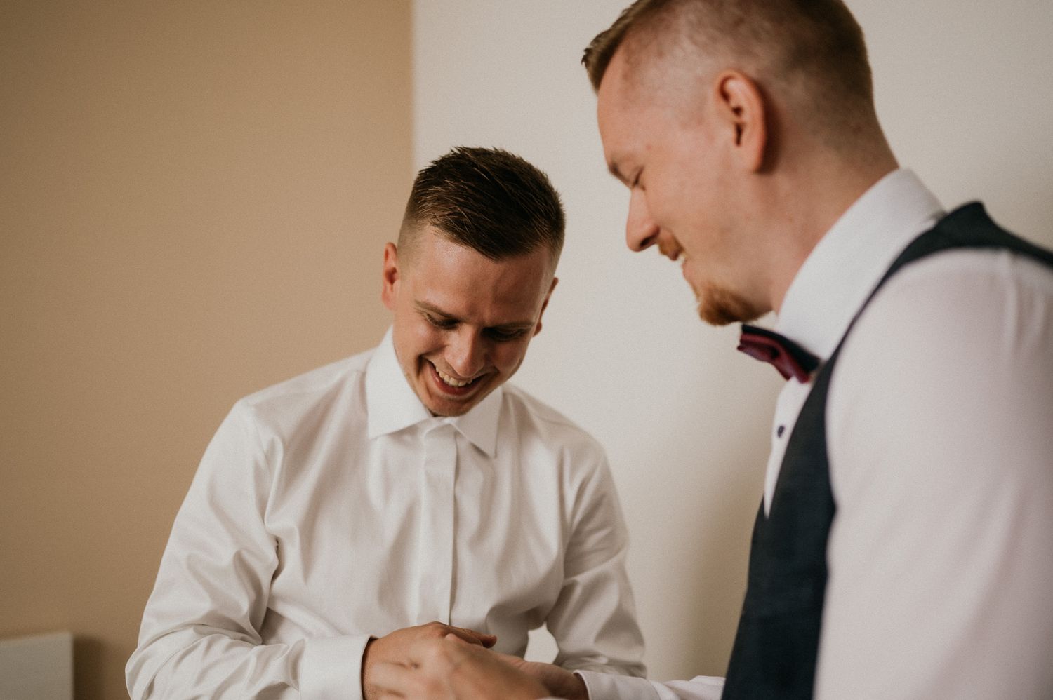 Two men in formal attire sharing a lighthearted moment while getting ready.