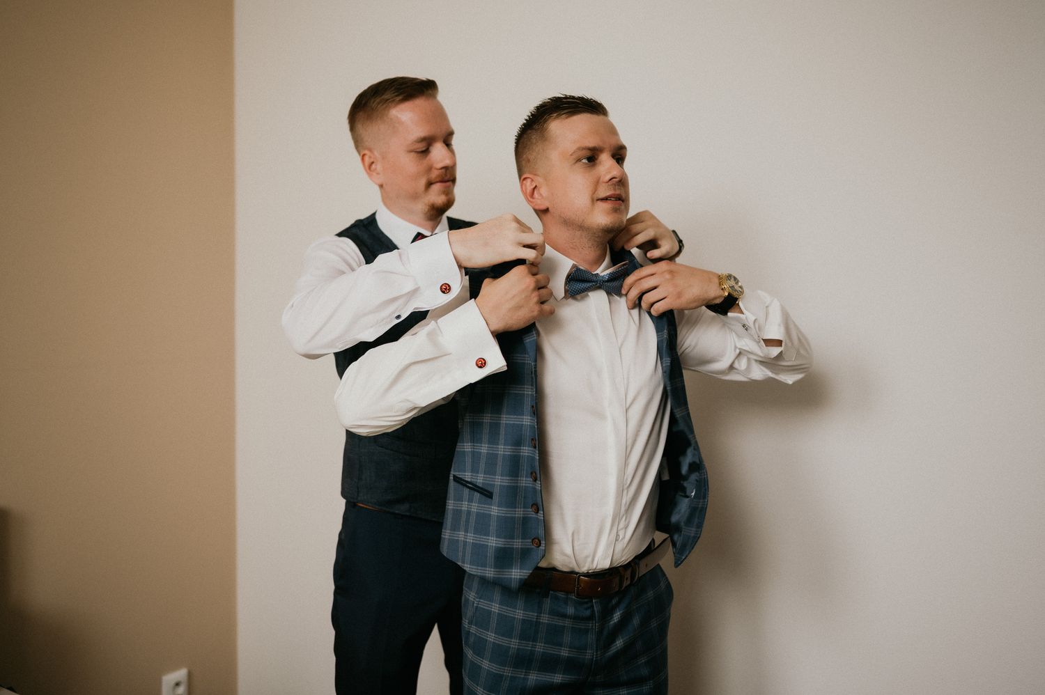Groomsmen in formal attire adjusting each other's bow ties before the ceremony.