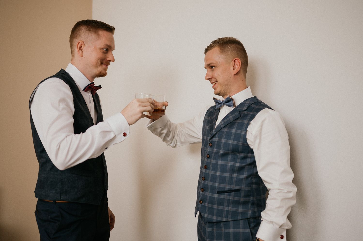 Groomsmen in matching vests sharing a toast with shot glasses during wedding preparations.