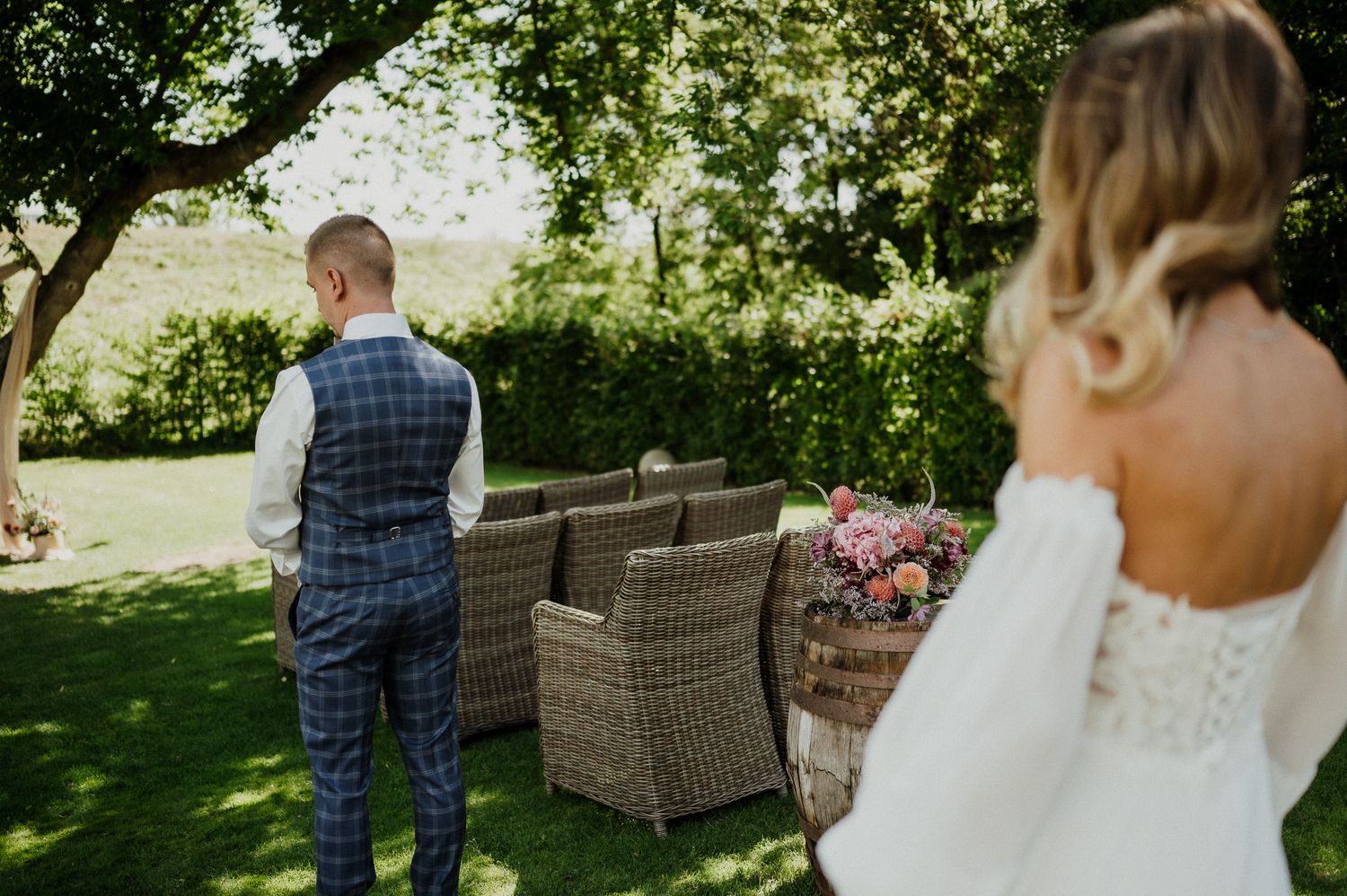 Couple stands in a garden setting with wicker furniture during a first look moment at their wedding.