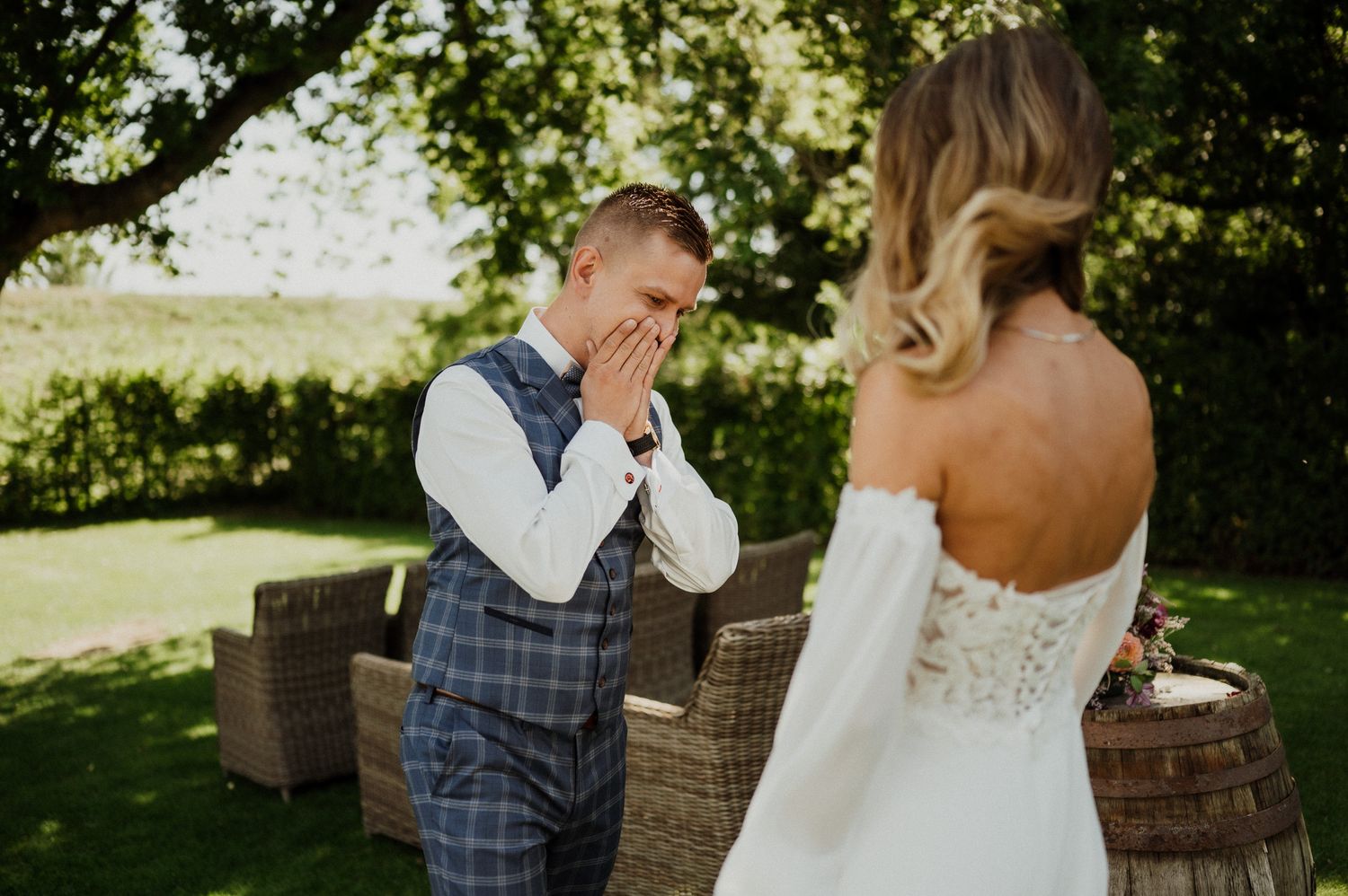 Groom shows emotional reaction during first look with bride in sunny garden setting.