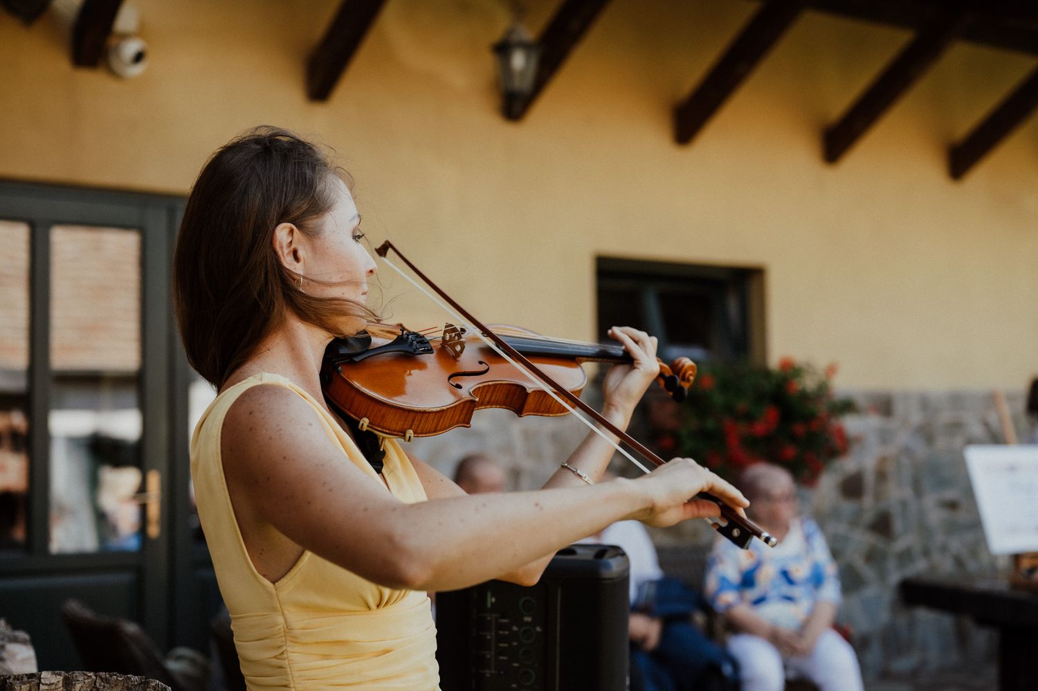 Violinist performs at outdoor wedding reception in yellow dress.