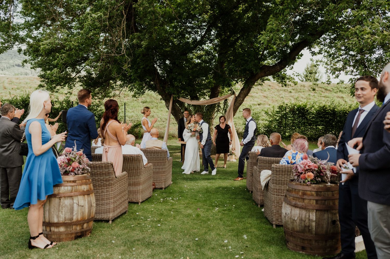 Wedding guests line rustic barrel seating arrangements in a garden ceremony setting.