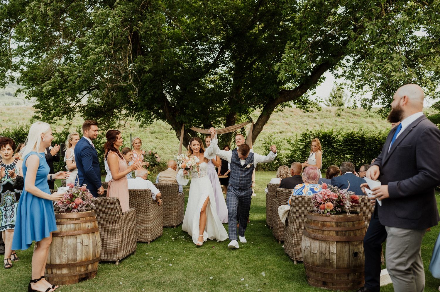 Guests celebrate at an outdoor wedding with rustic barrel seating and natural decor.