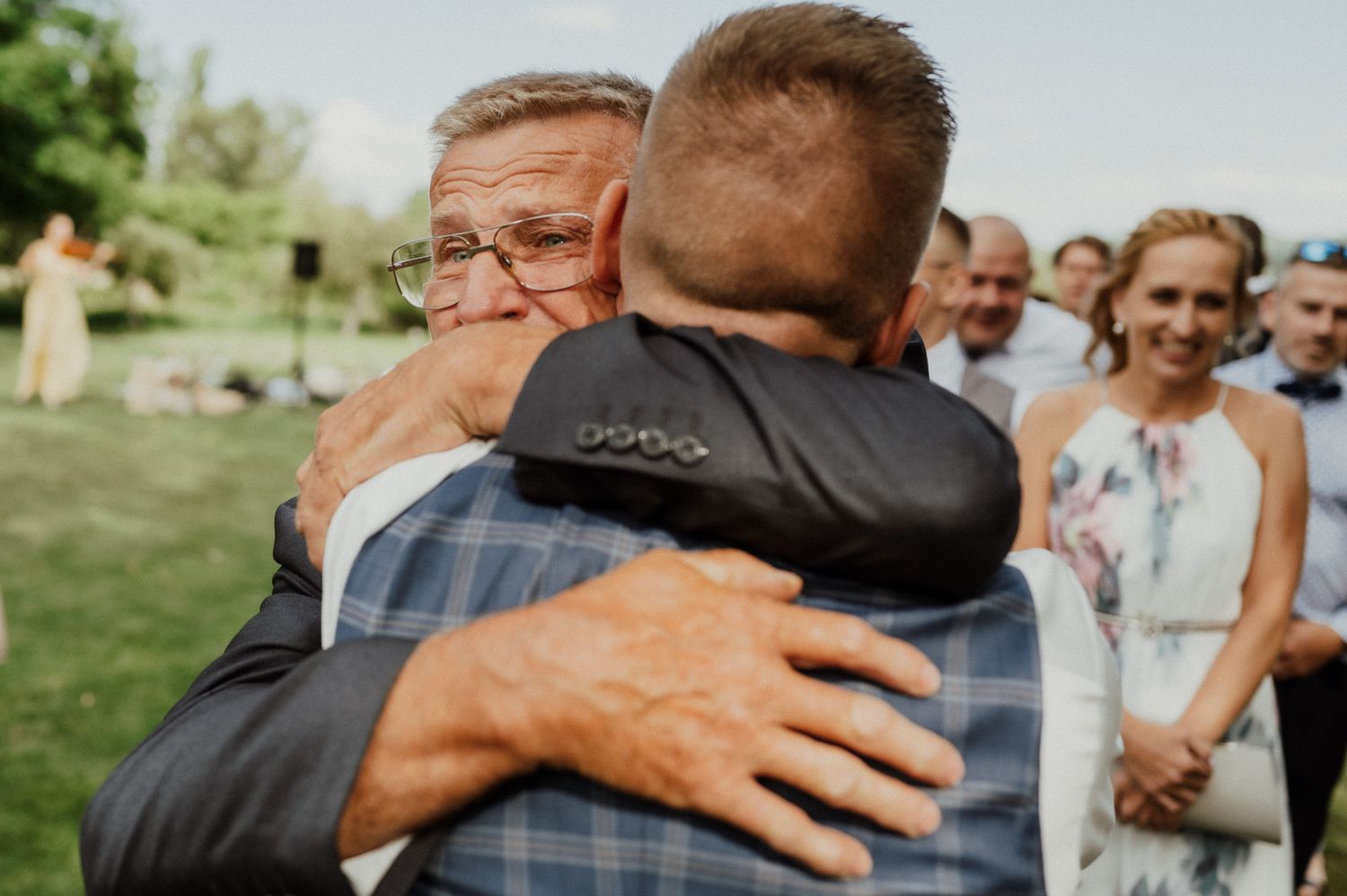 Tearful emotional embrace during outdoor wedding ceremony with guests watching.