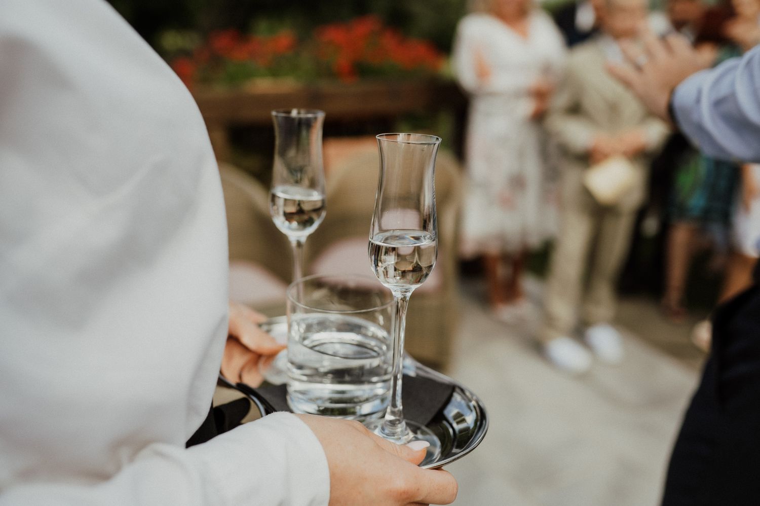 Close up of champagne glasses being carried on serving tray at outdoor event.