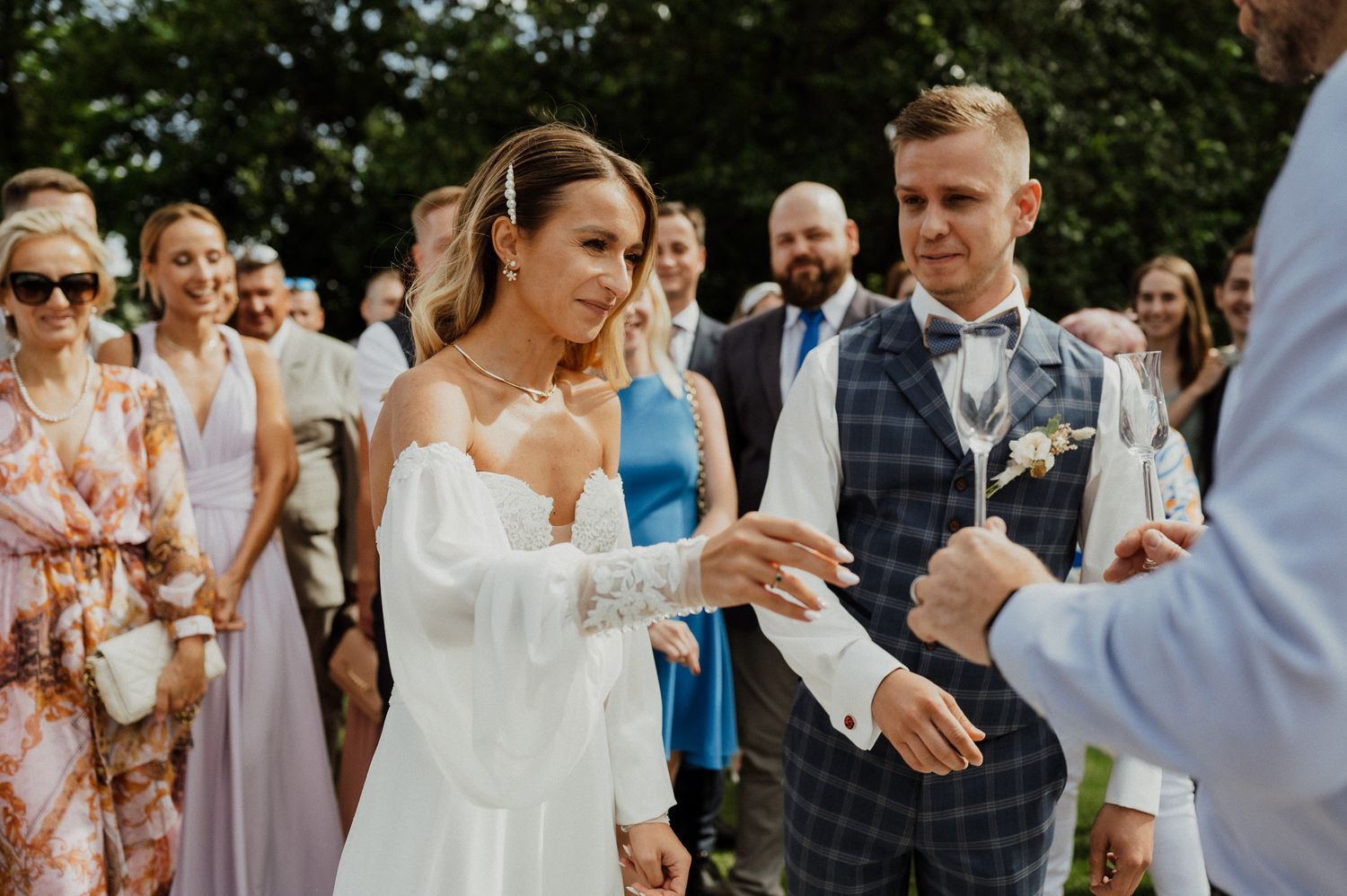 Couple participates in wedding ceremony ritual outdoors surrounded by guests.