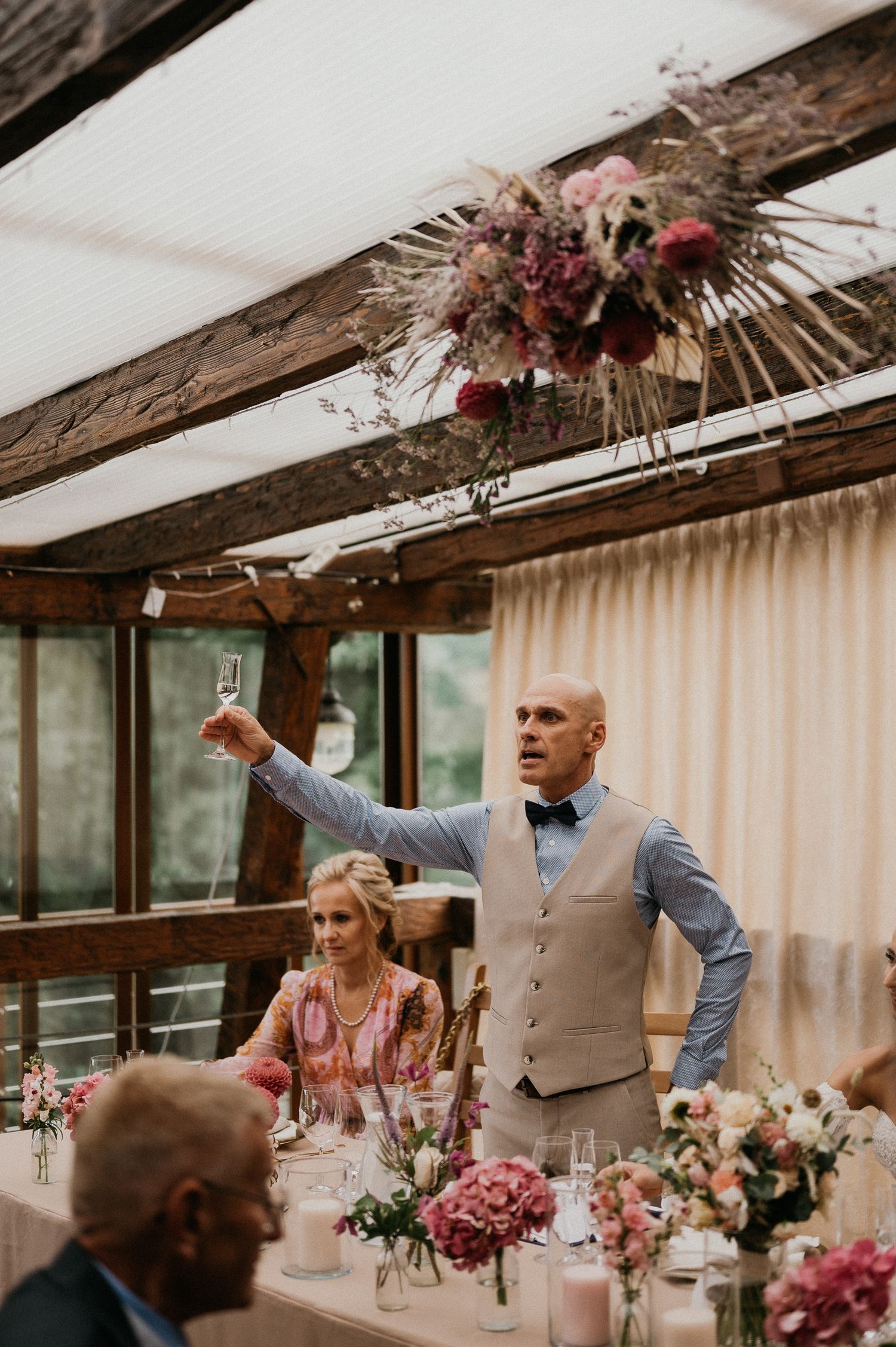 Rustic wedding reception venue with dried floral arrangements hanging from wooden ceiling beams.