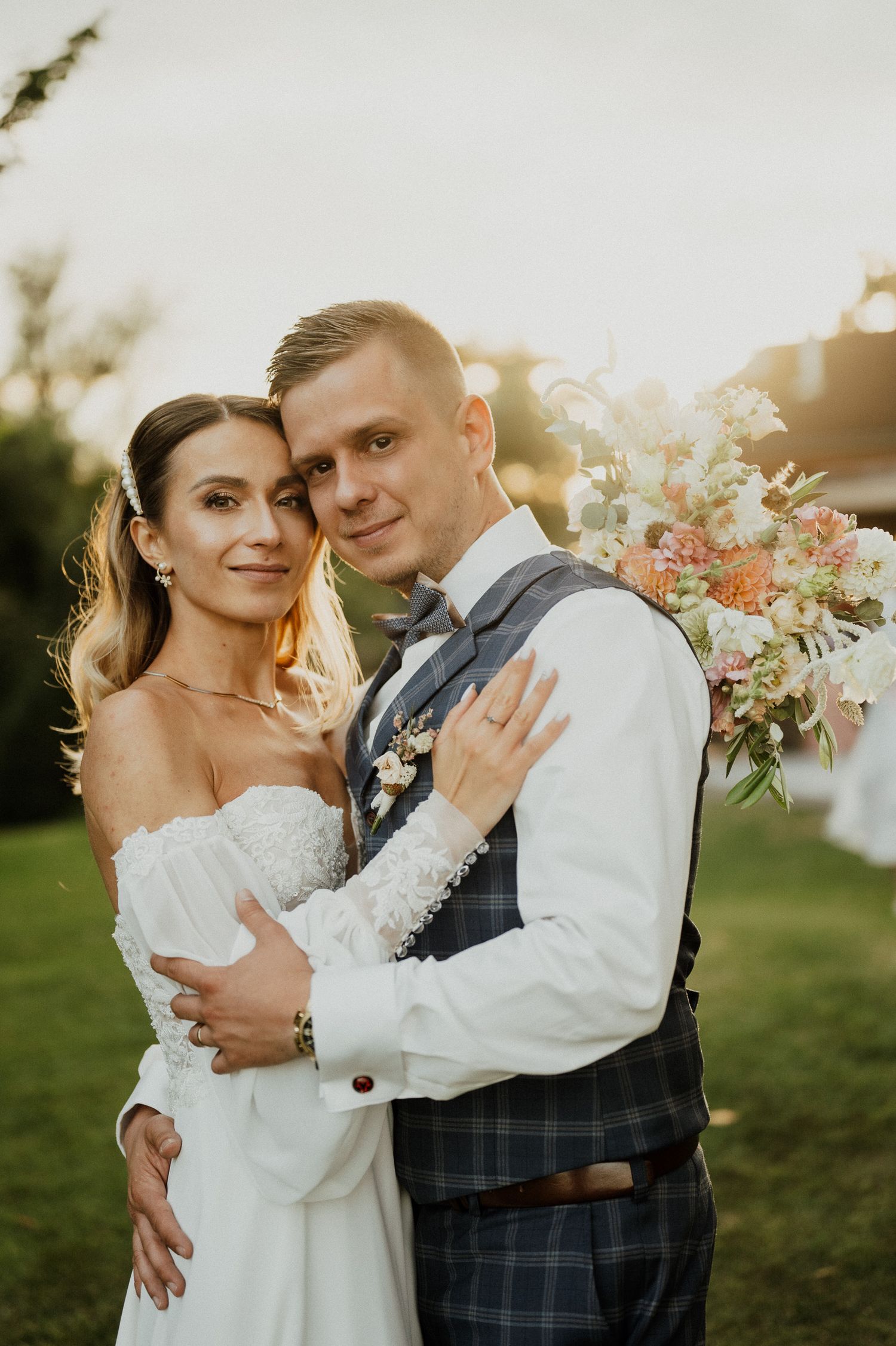 A romantic wedding portrait of a couple embracing at sunset with a beautiful floral bouquet.