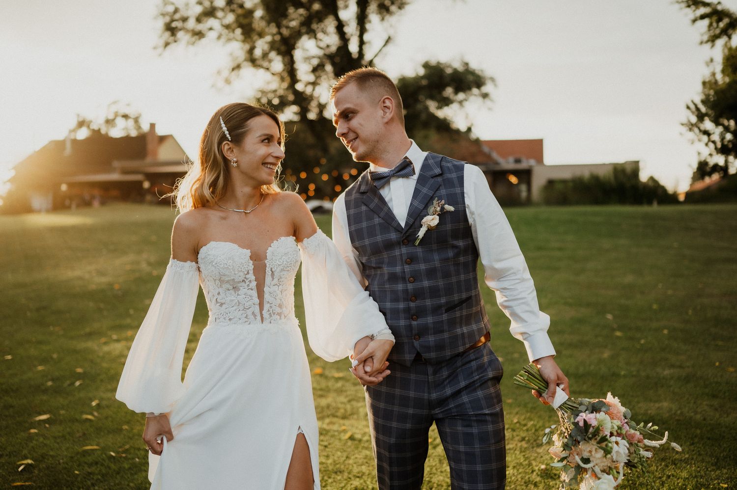 A joyful wedding couple walking together at sunset in an outdoor garden setting.