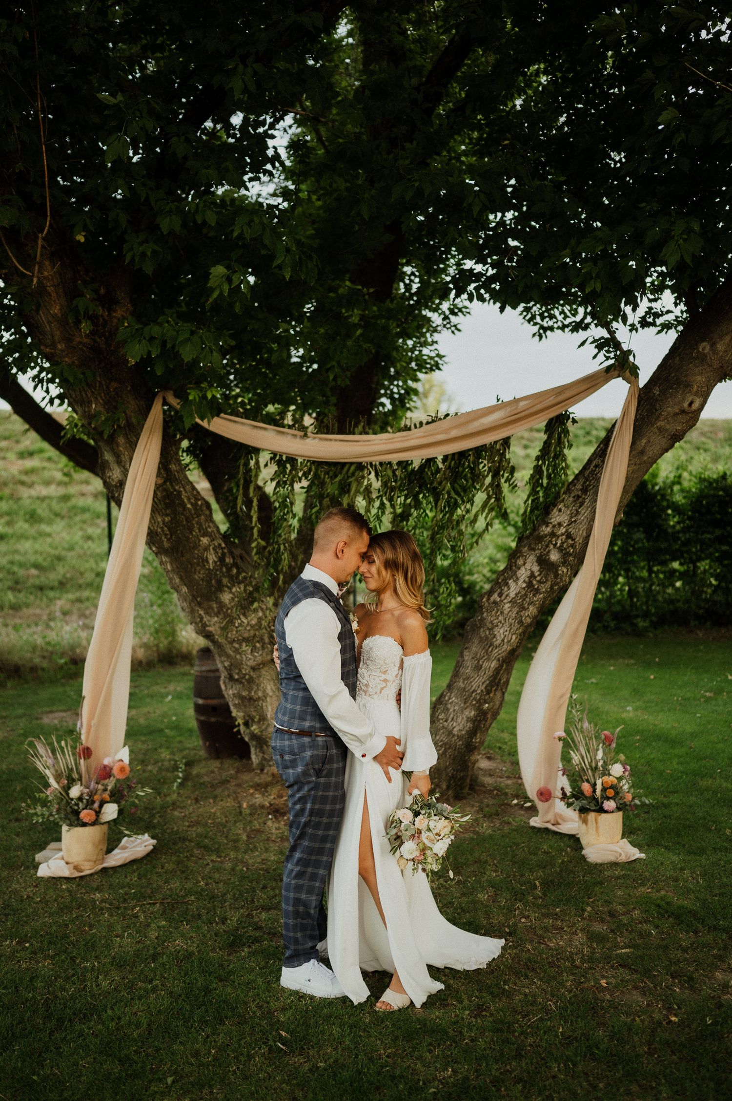 A romantic wedding ceremony setup under a tree with flowing fabric and floral decorations.