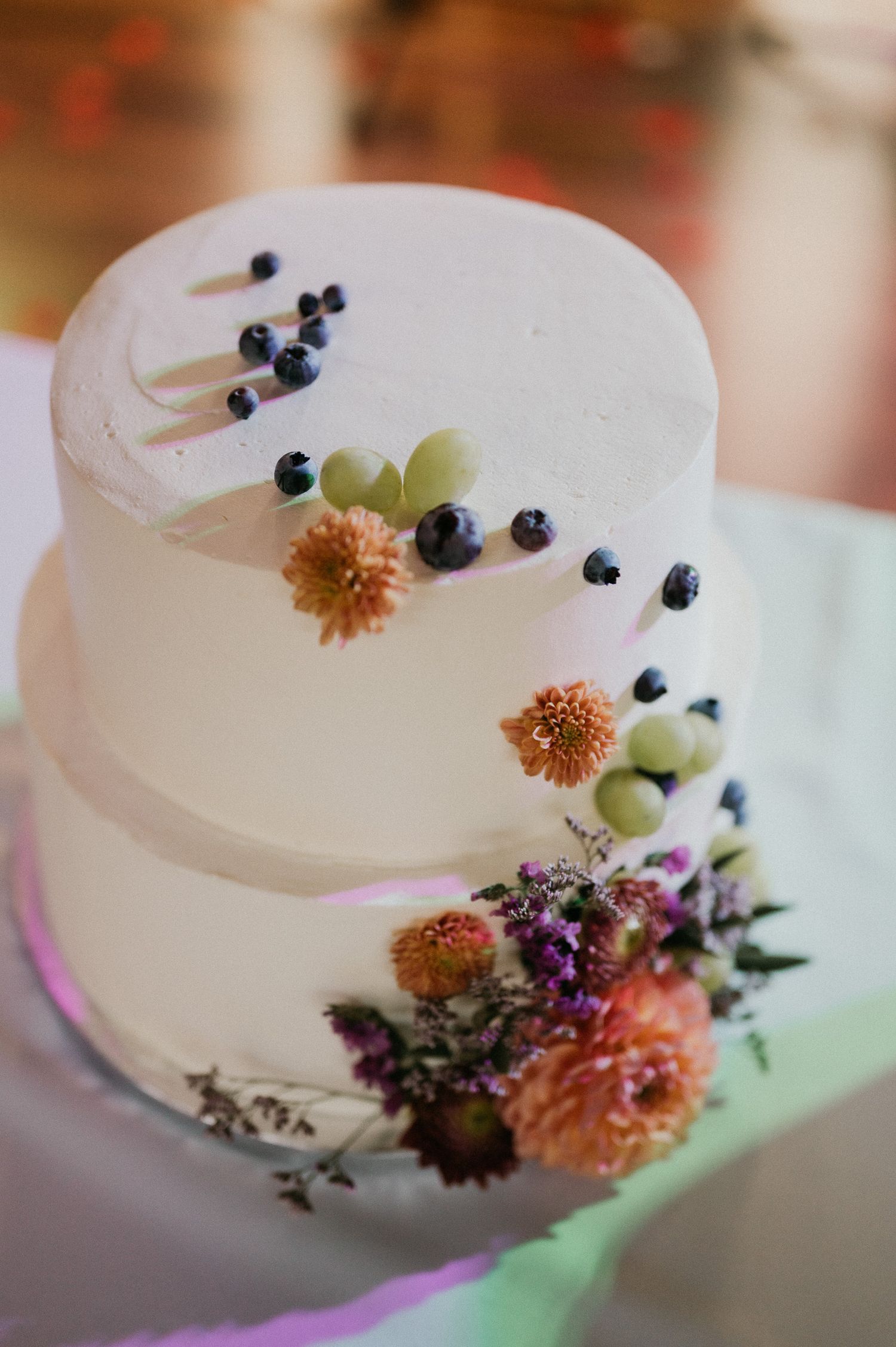 An elegant white wedding cake decorated with fresh blueberries and coral-colored flowers.