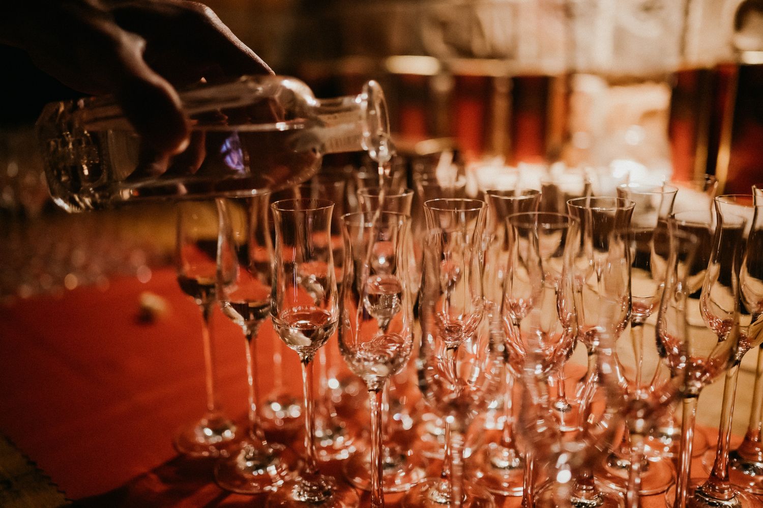 Wine glasses lined up on a bar being filled during a service event.