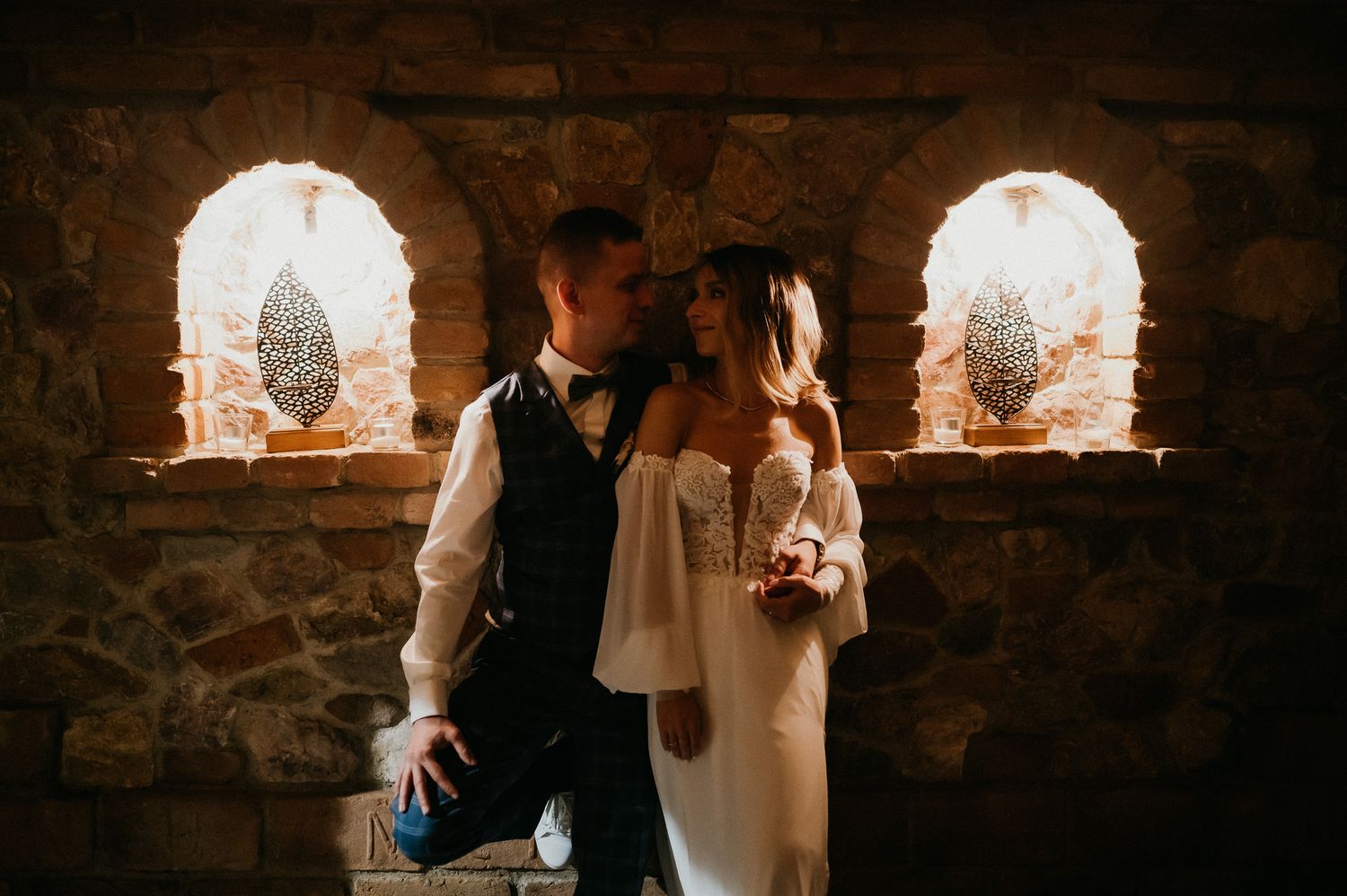 Couple posing in front of illuminated stone archways with decorative elements.