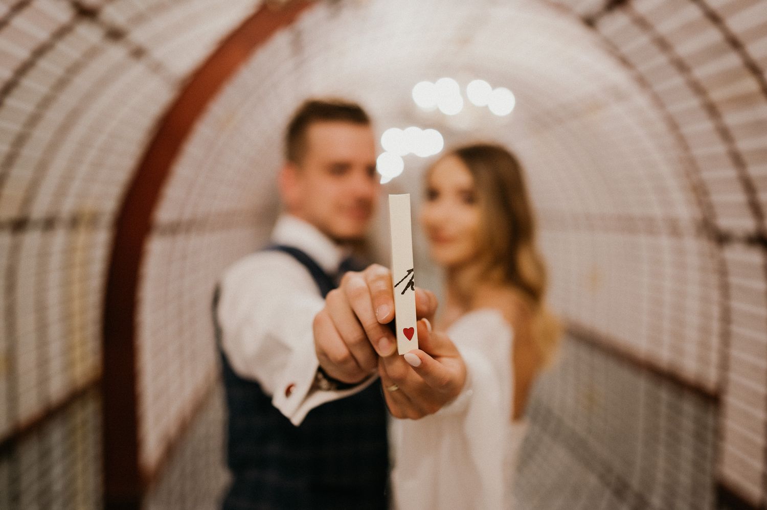 Couple shows off engagement ring in a dimly lit tunnel with elegant arched architecture.