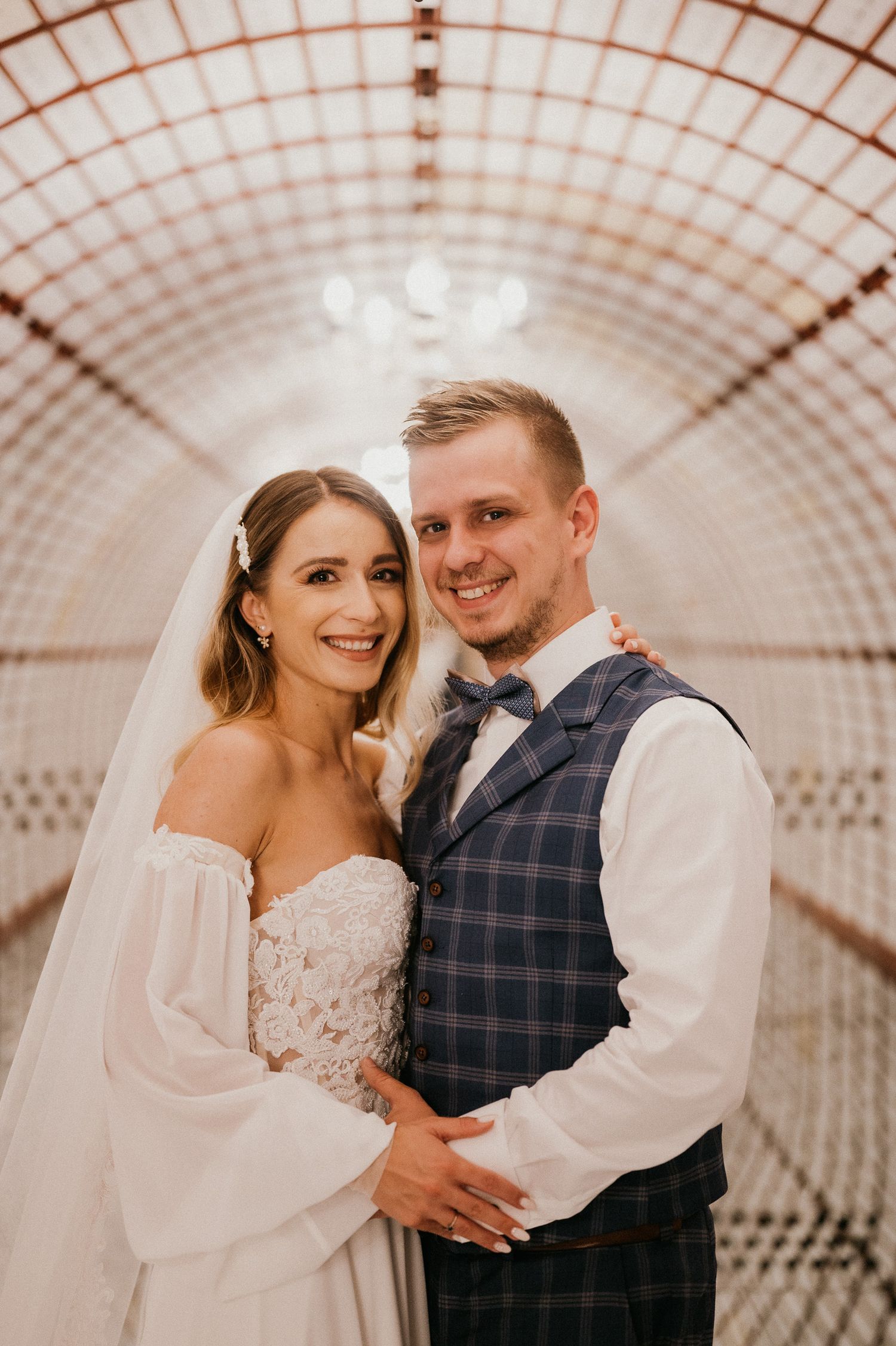 Joyful wedding portrait in elegant tunnel with geometric pattern ceiling.