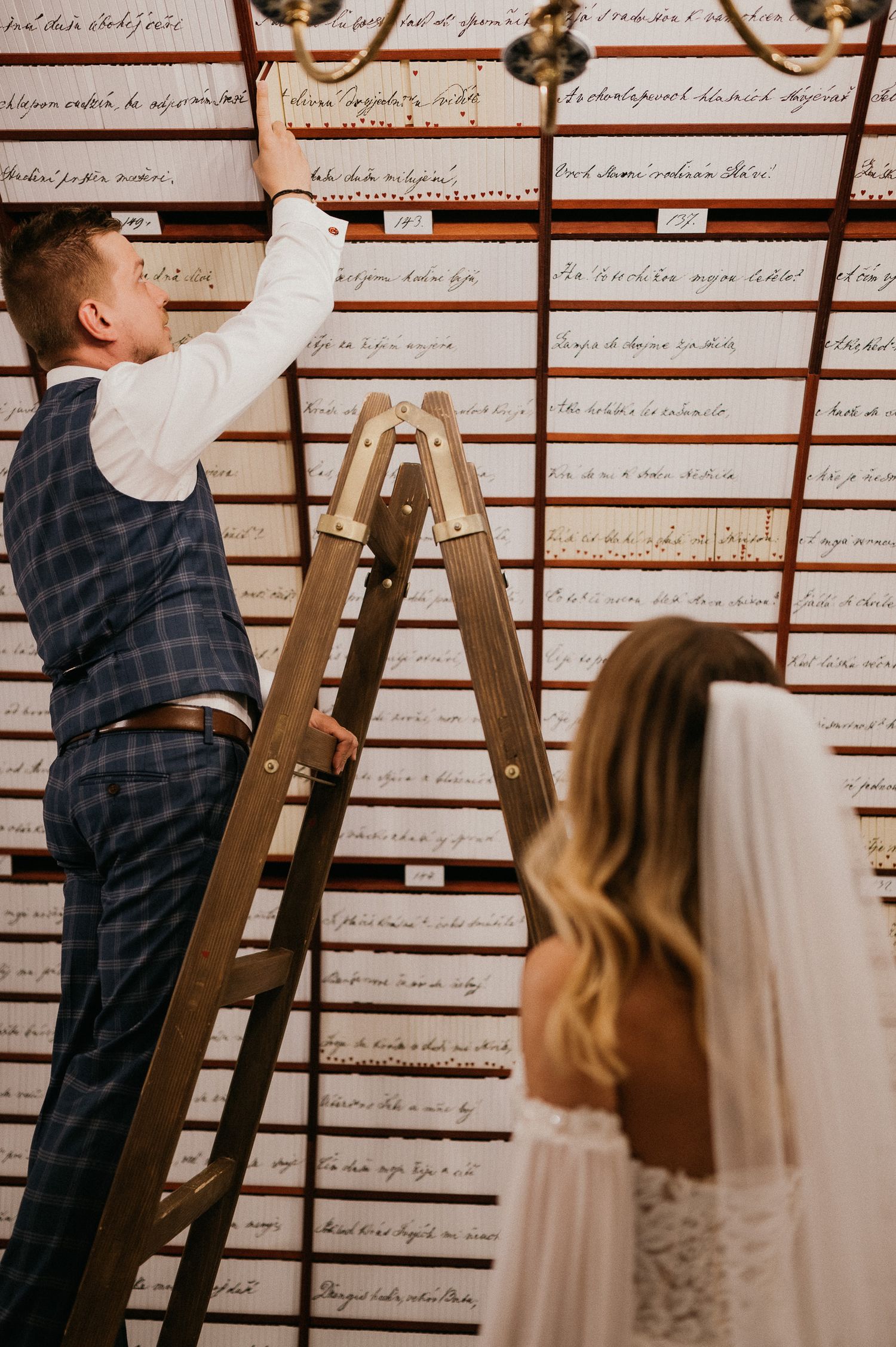 Wedding couple exploring historic document wall with wooden ladder.