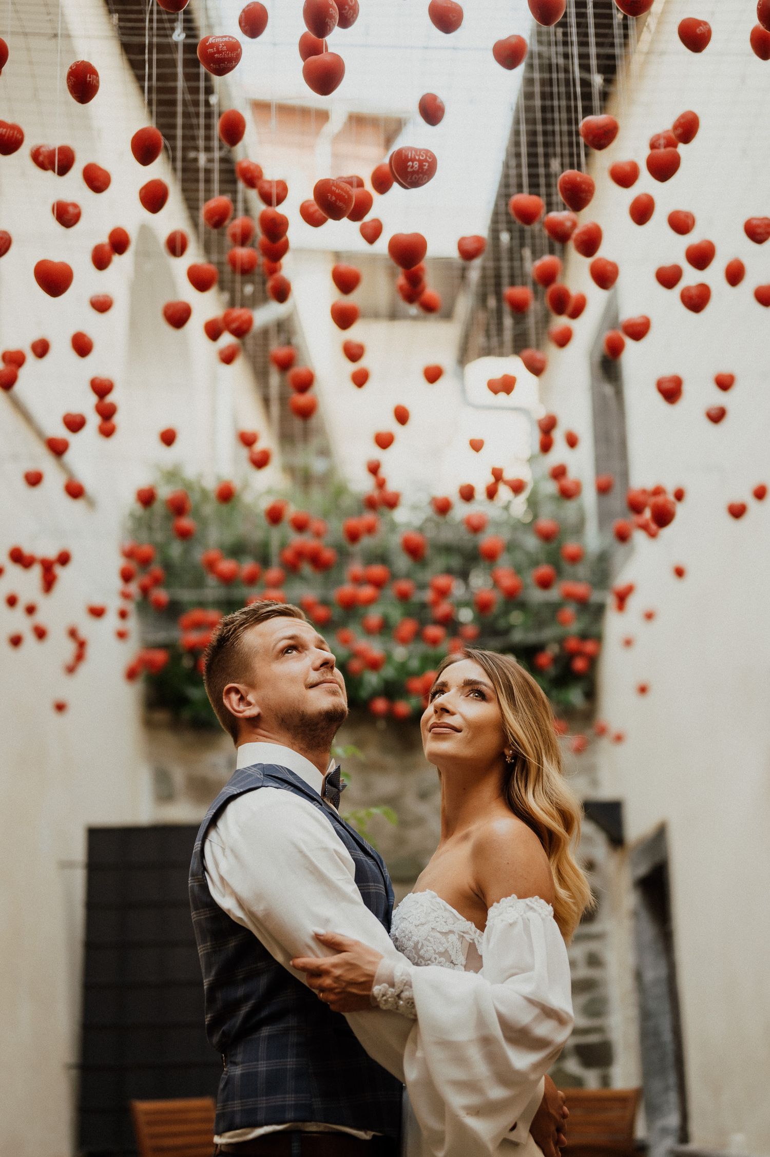 Romantic couple gazes up at floating red balloons in white space.