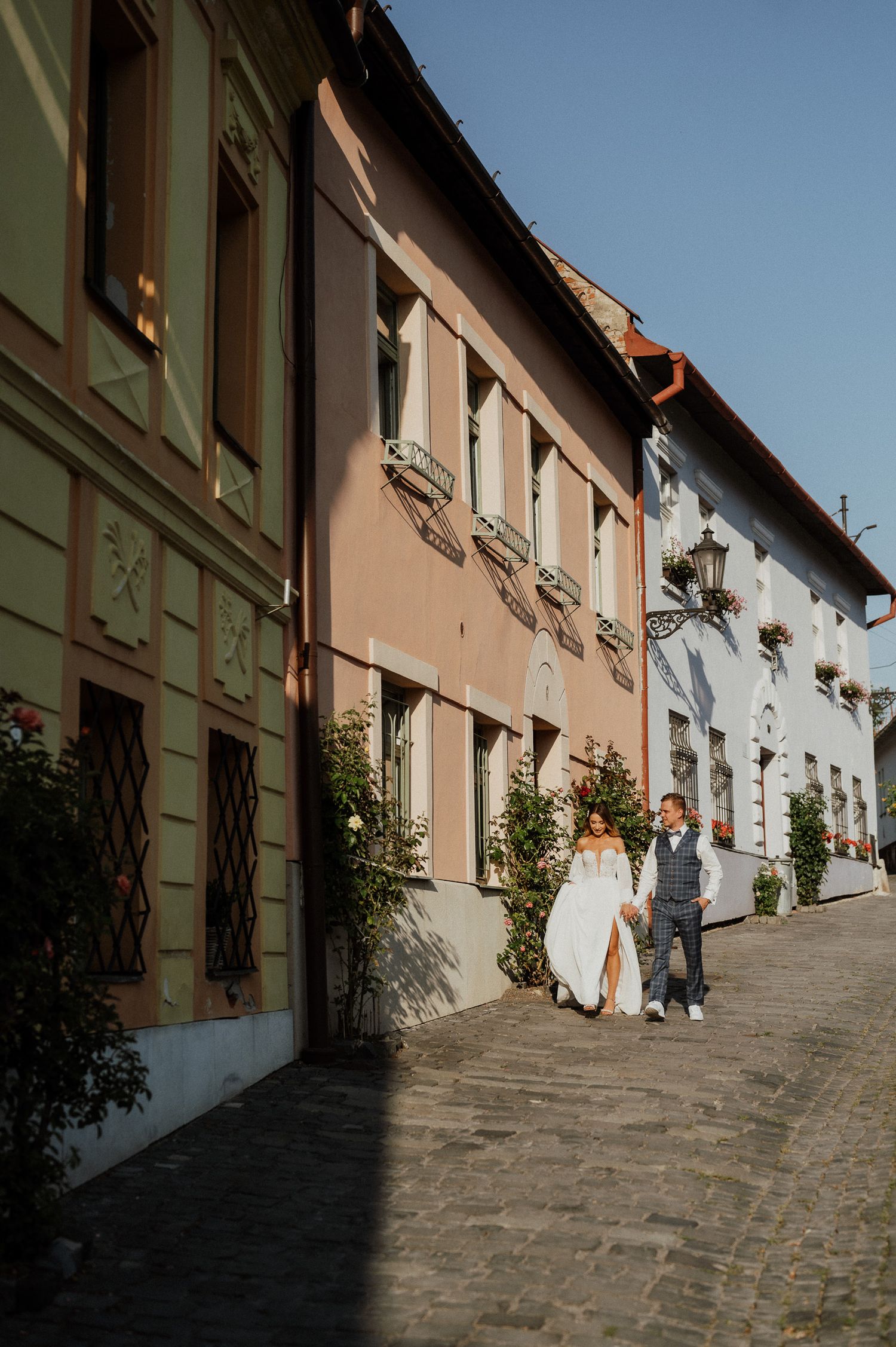 Couple strolls down colorful European street with pastel buildings and traditional architecture.