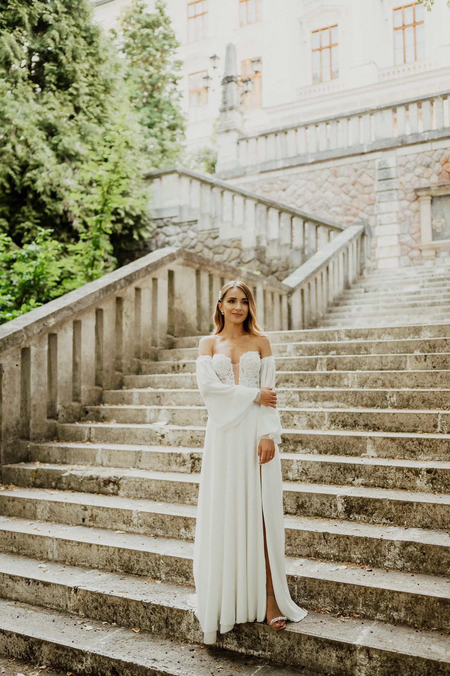 White gown against stone steps with classical architecture and greenery in background.