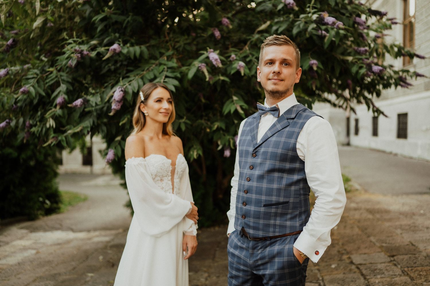 Wedding couple poses together outdoors with groom in vest and bride in flowing white dress.
