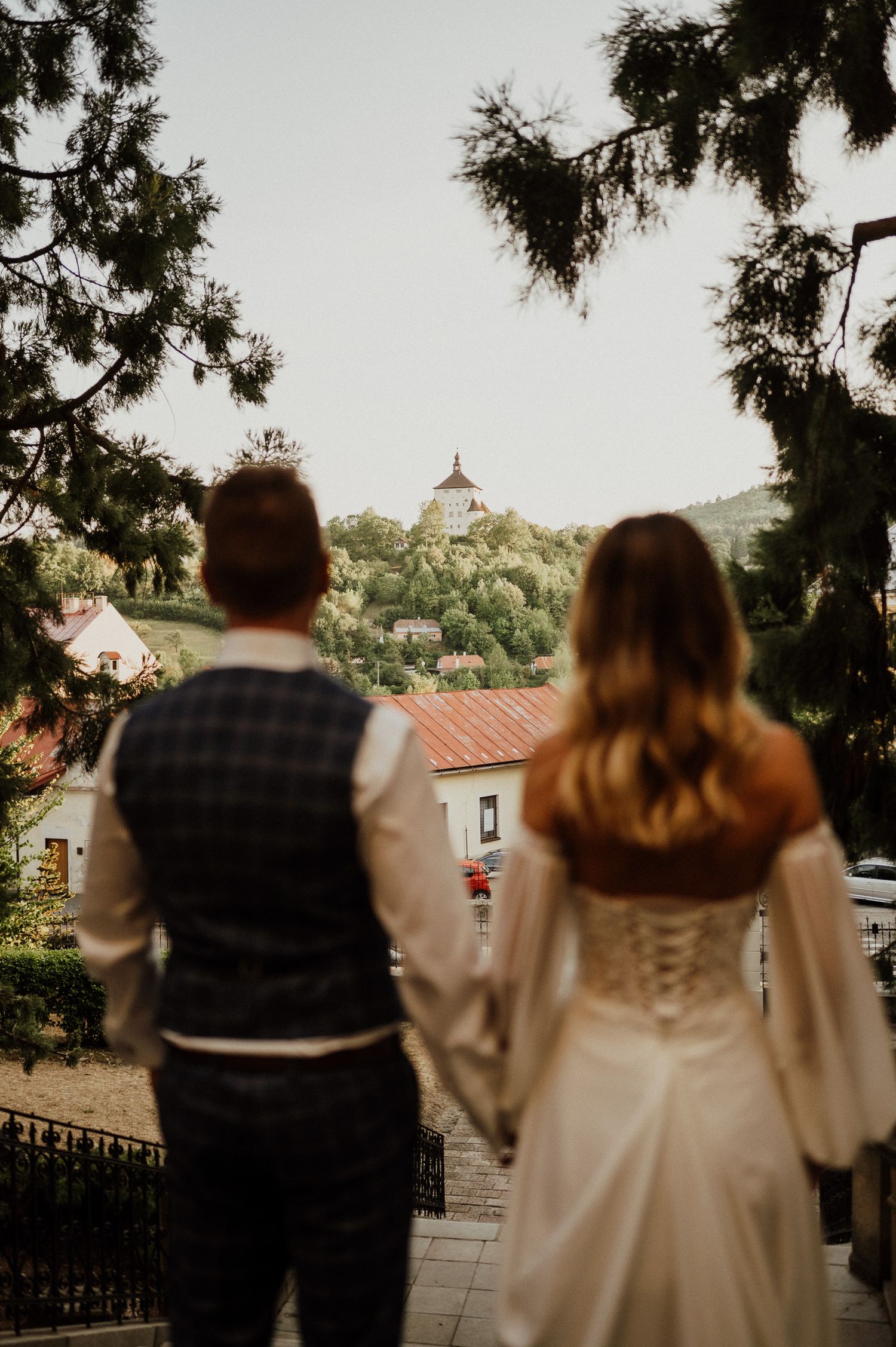 Wedding couple looks towards church spire on hilltop during sunset.