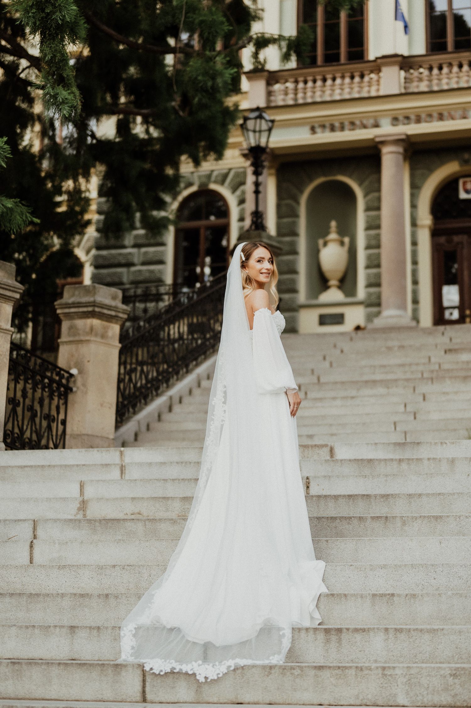 Ethereal bridal portrait on grand stone staircase showcasing flowing white wedding gown.