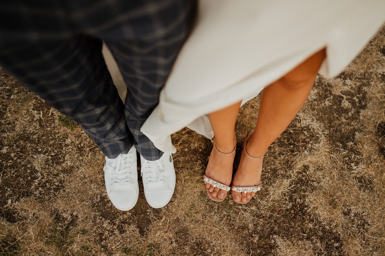 Close-up shot of wedding couple's contrasting footwear on dusty ground.