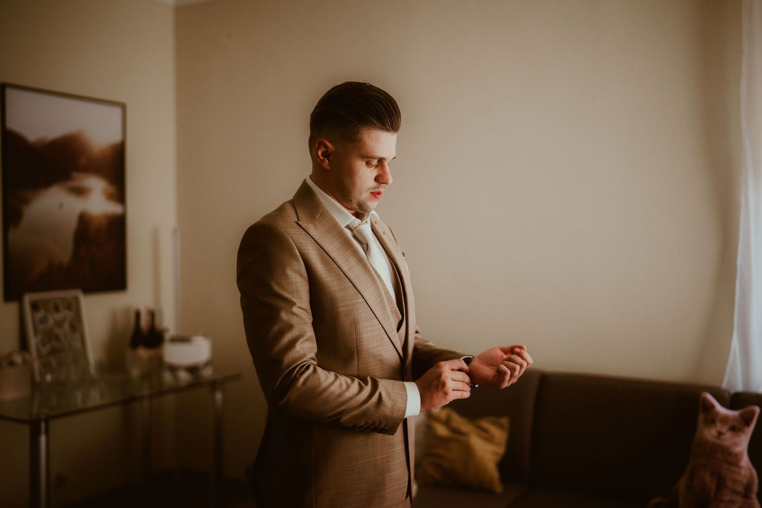 Person in tan suit examining something in their hands while standing in a minimalist room.