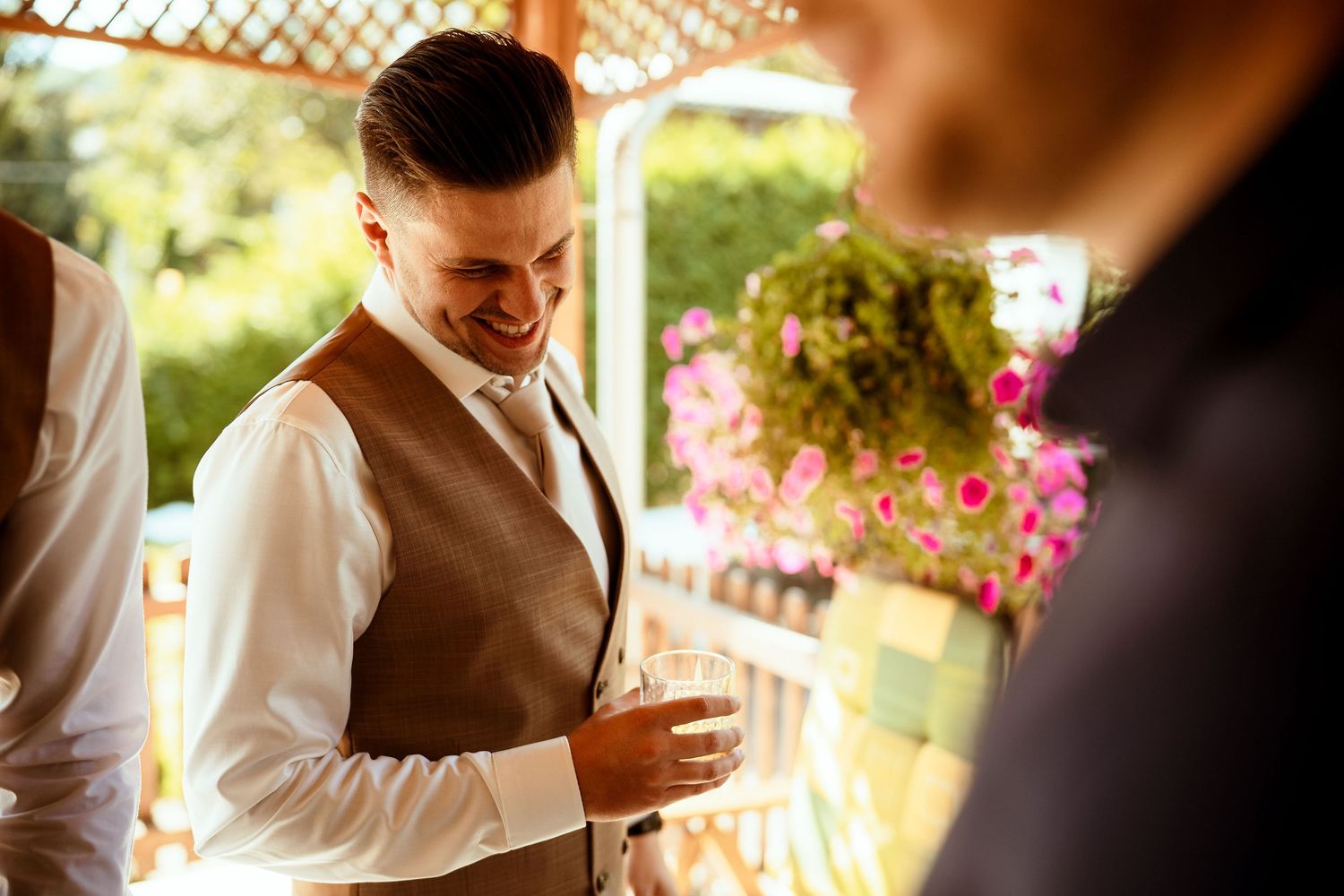 A stylishly dressed person in a brown vest and white shirt checks their phone in a garden setting.