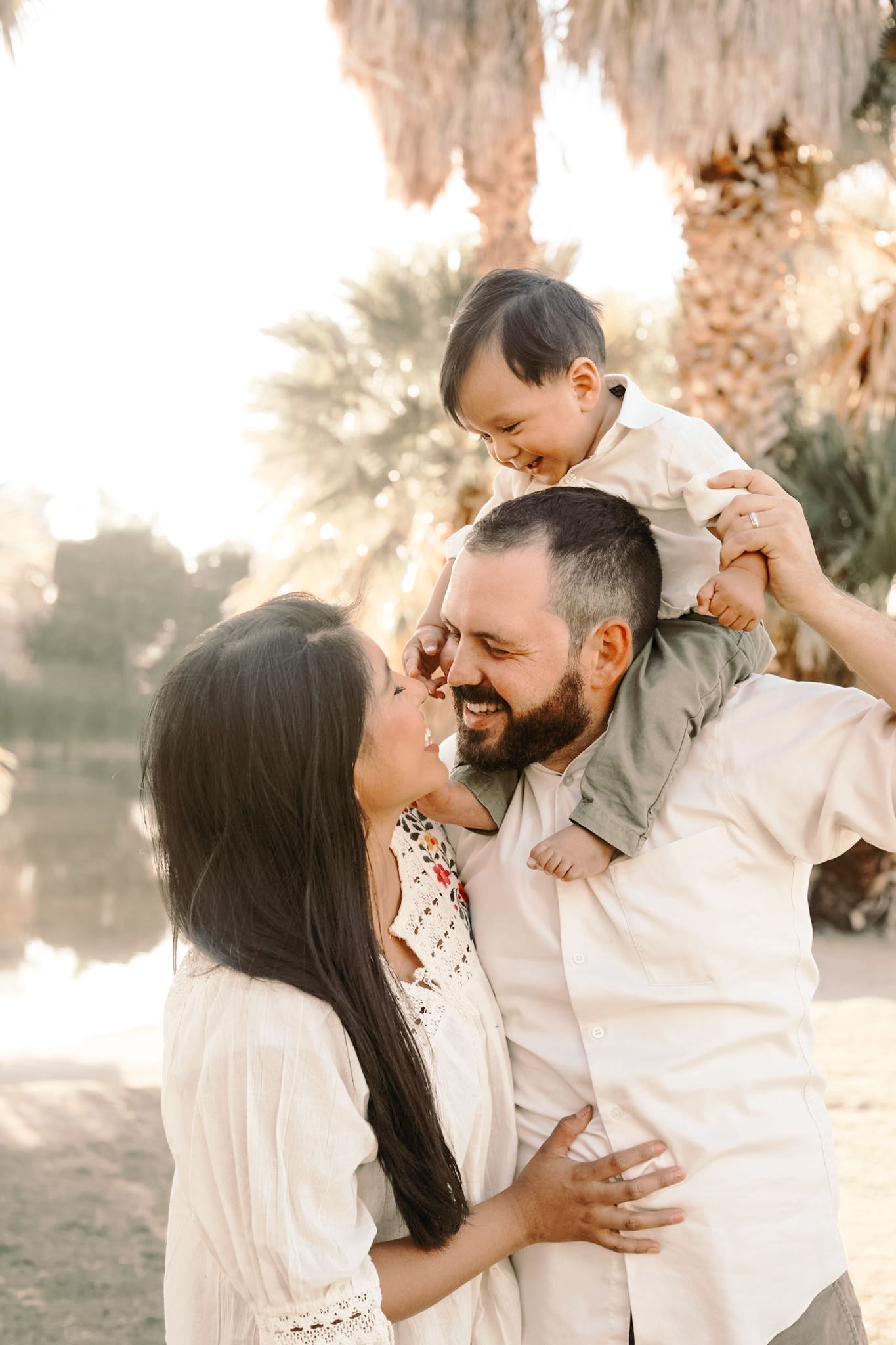 Tucson family photographer captures joyful outdoor moment with parents and their toddler sitting on dad’s shoulders at sunset.