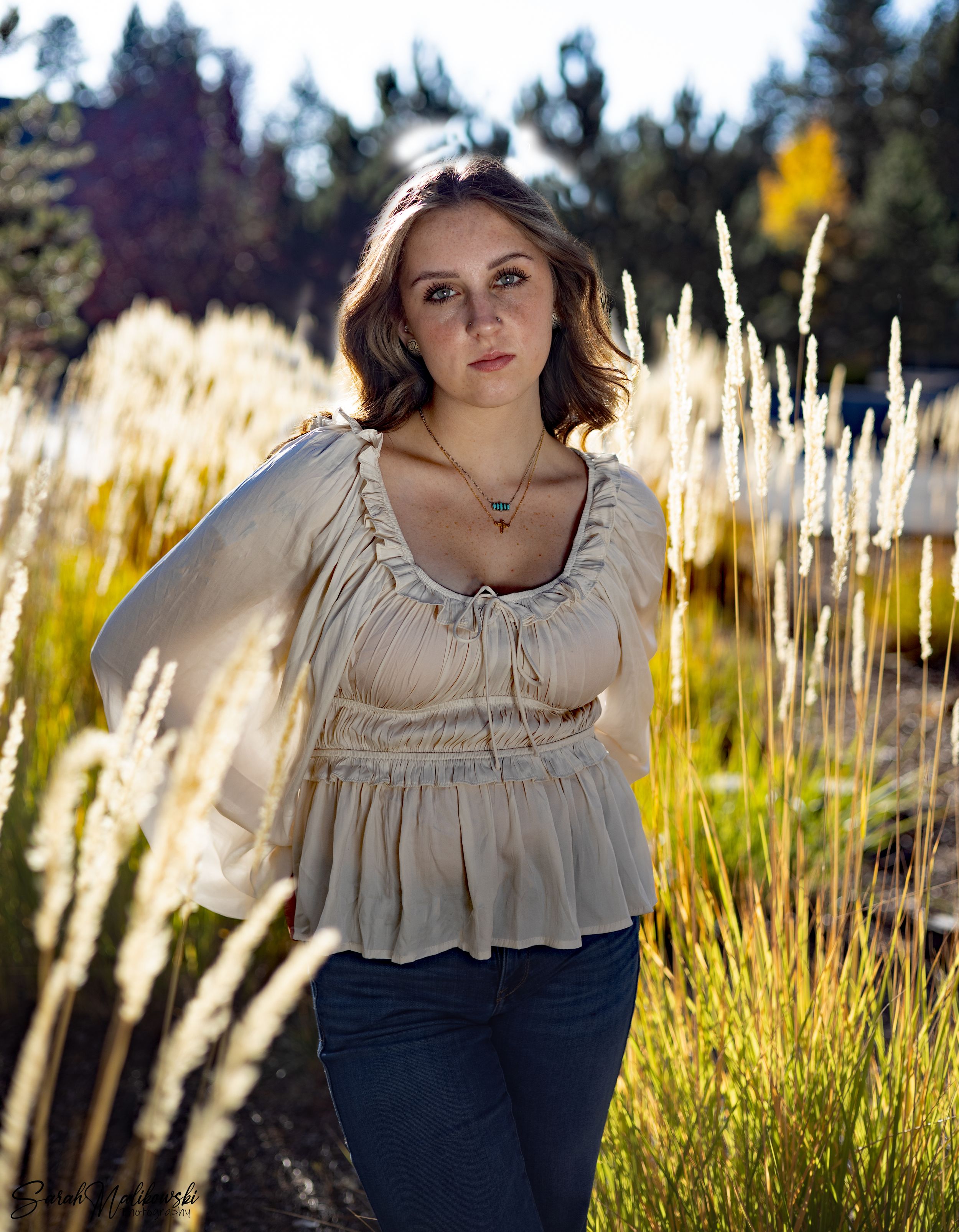 Portrait in beige peasant top against sunlit grass background.
