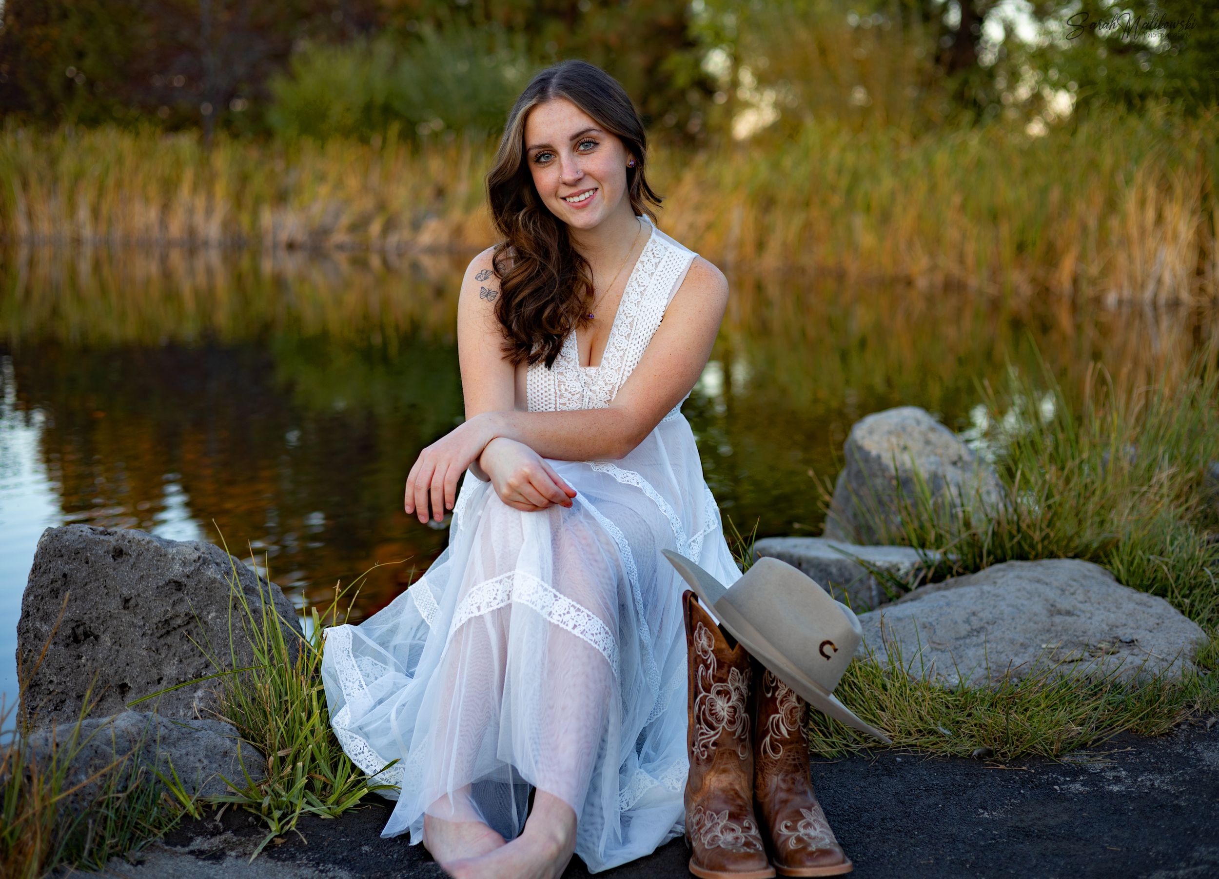 Person in white dress sitting on rocks by water.
