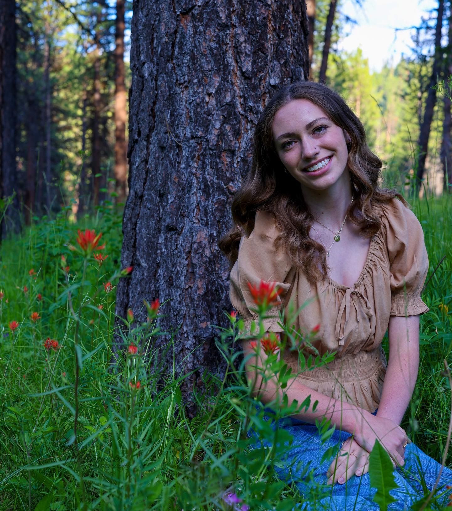 Natural outdoor portrait by pine tree with wildflowers in forest setting.