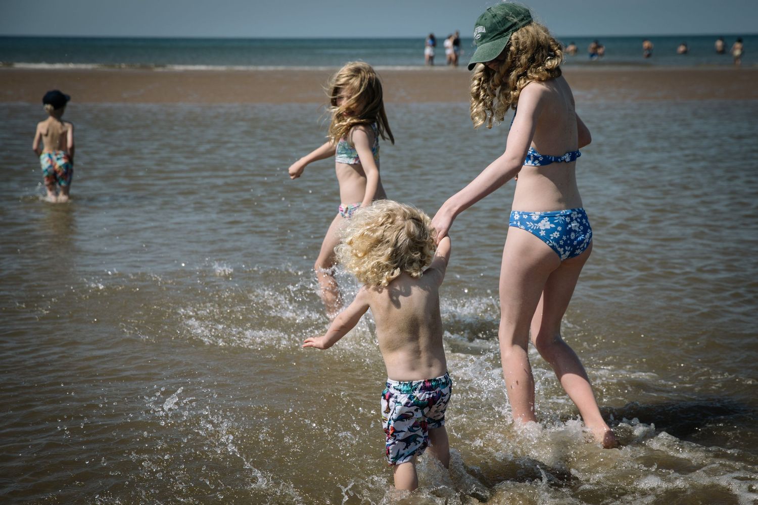 Family members splashing and playing together in shallow ocean water on a sunny beach day.