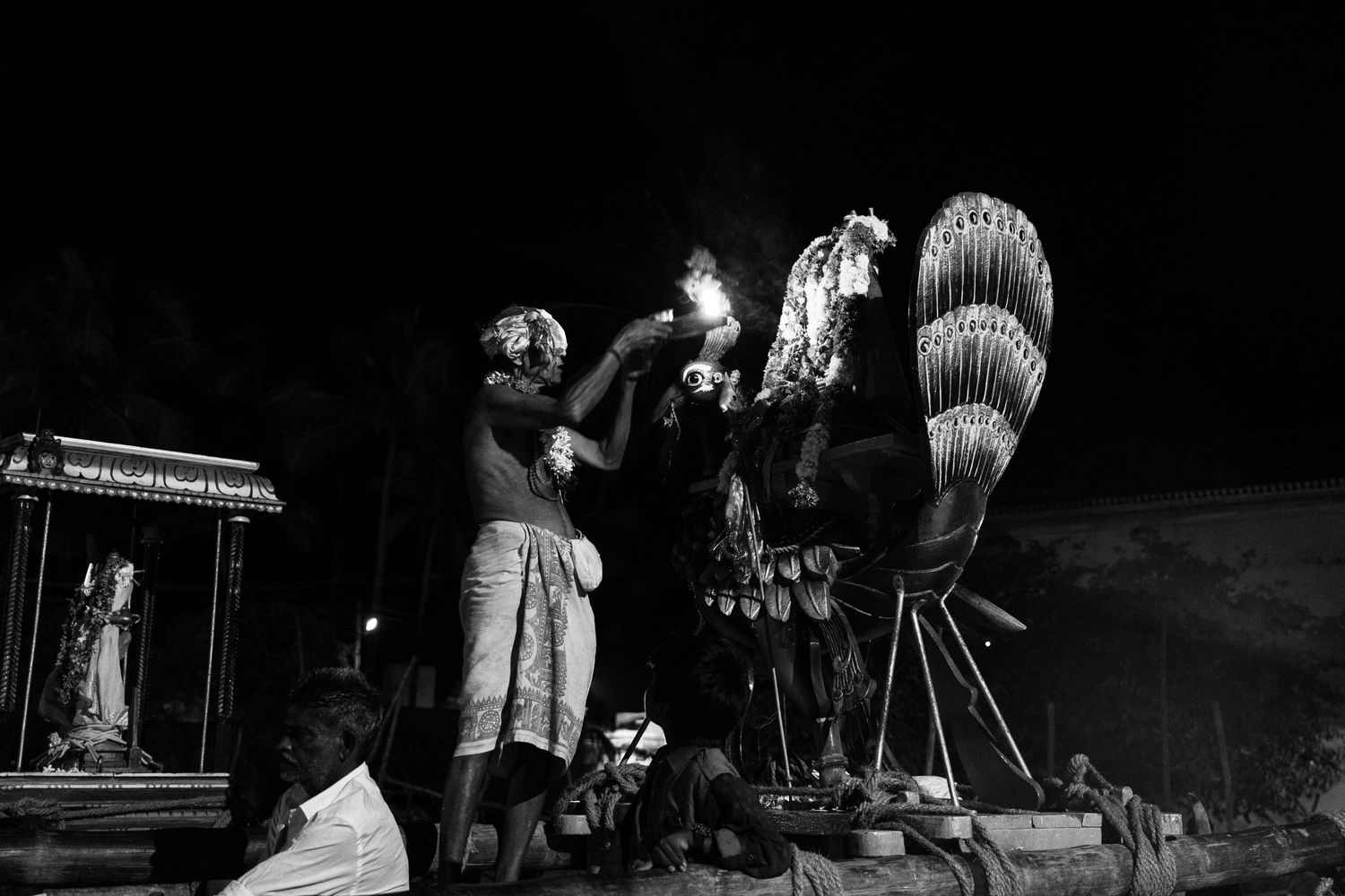 Traditional Hawaiian ceremony featuring performers and kahili standards under night sky.