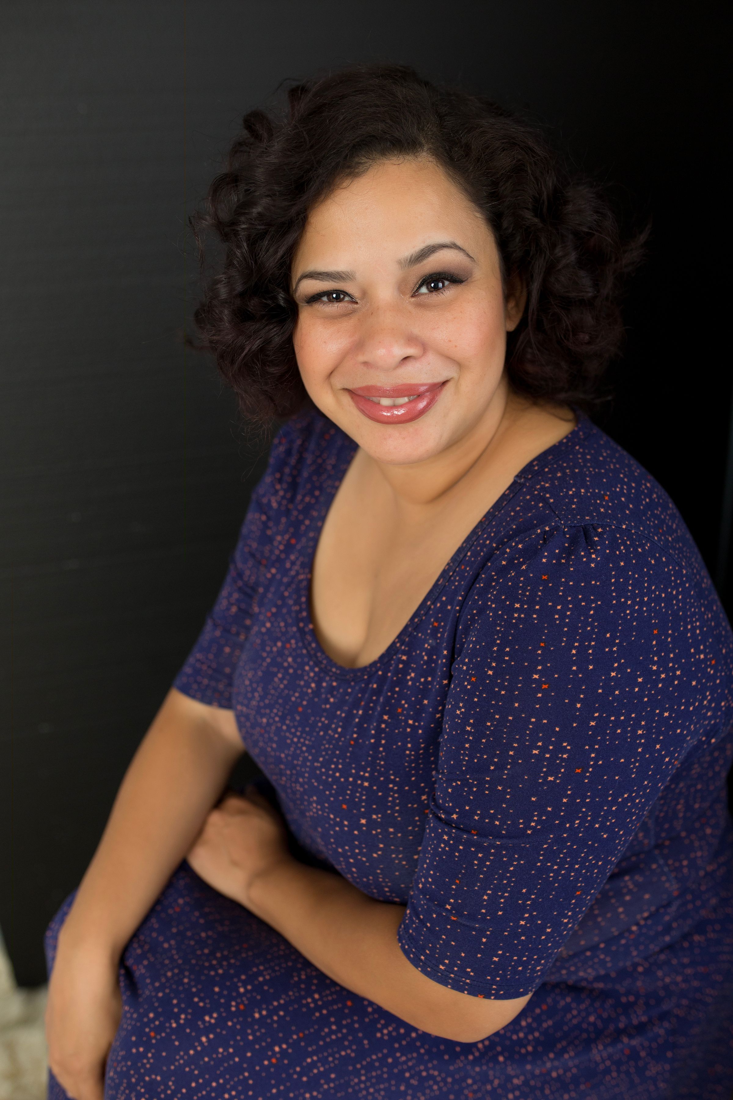 Studio portrait against dark background featuring person in sparkly navy dress with curly hair.