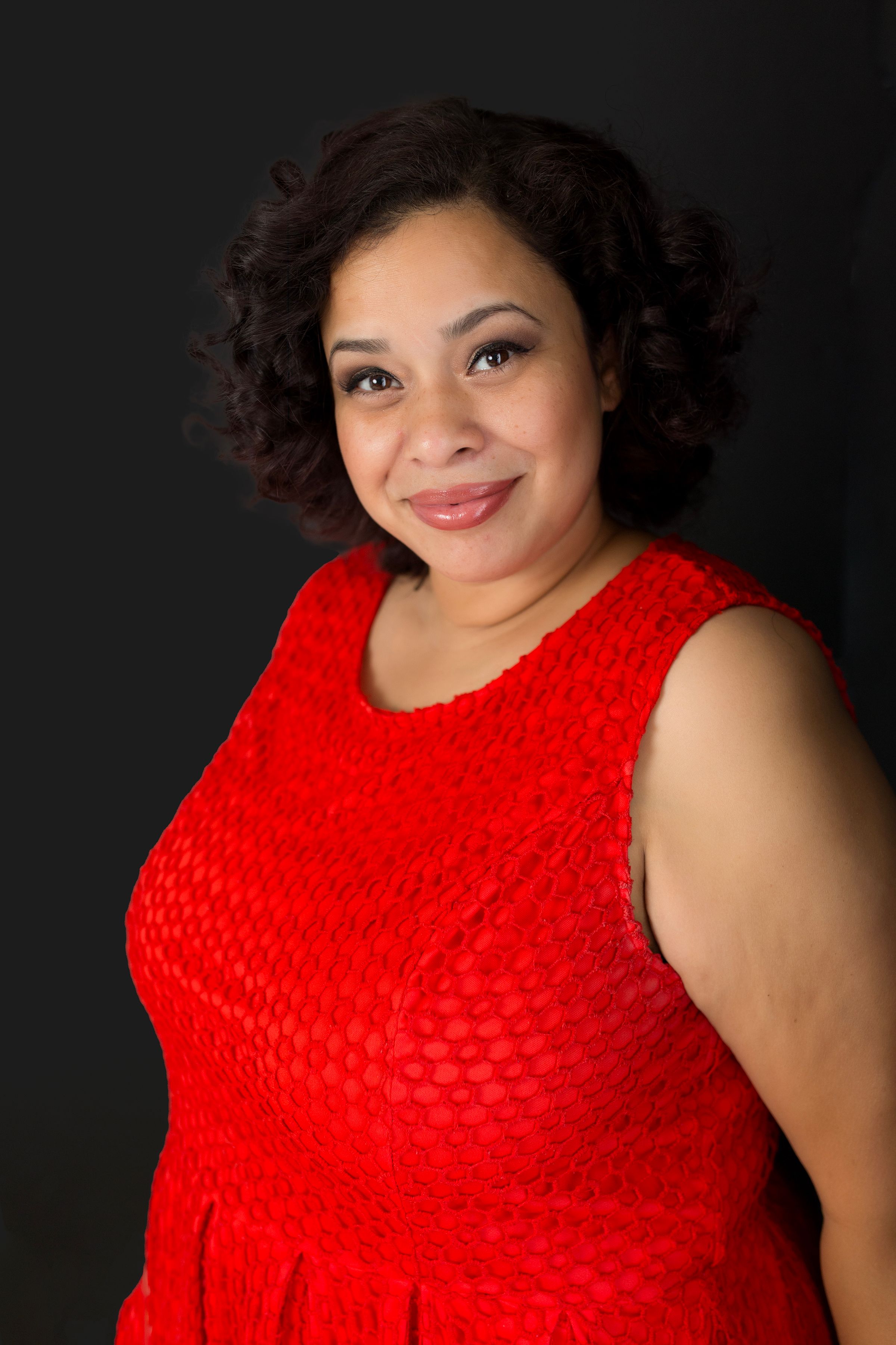 Studio portrait featuring person in bright red textured dress against dark background.