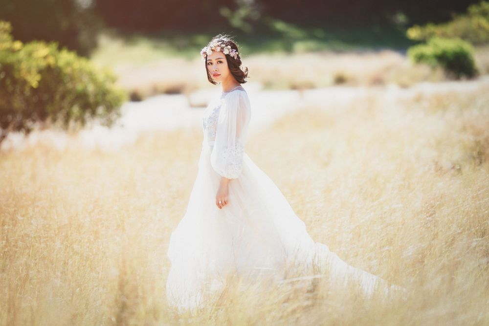 Bride in white tulle gown and floral crown walking through golden wheat fields.