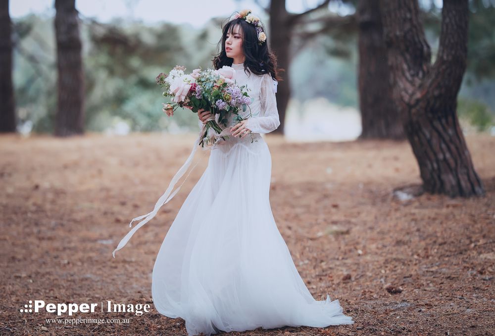Elegant bride in lace gown holding a wildflower bouquet among pine trees.
