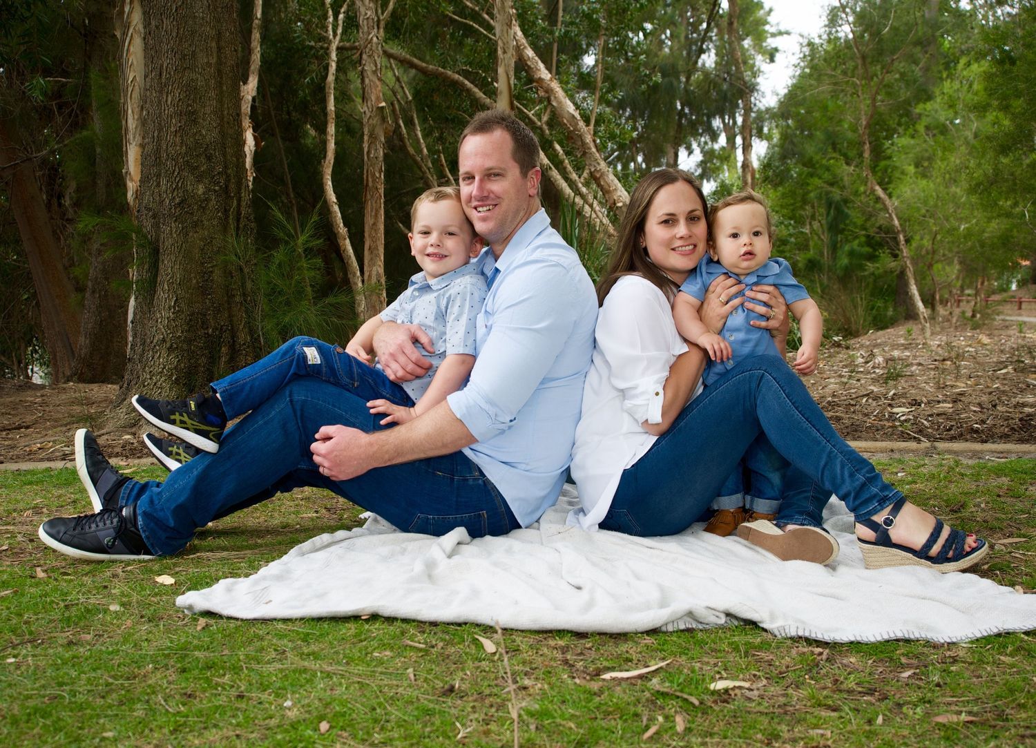 mother and father sitting on the groung at a park holding their two young children