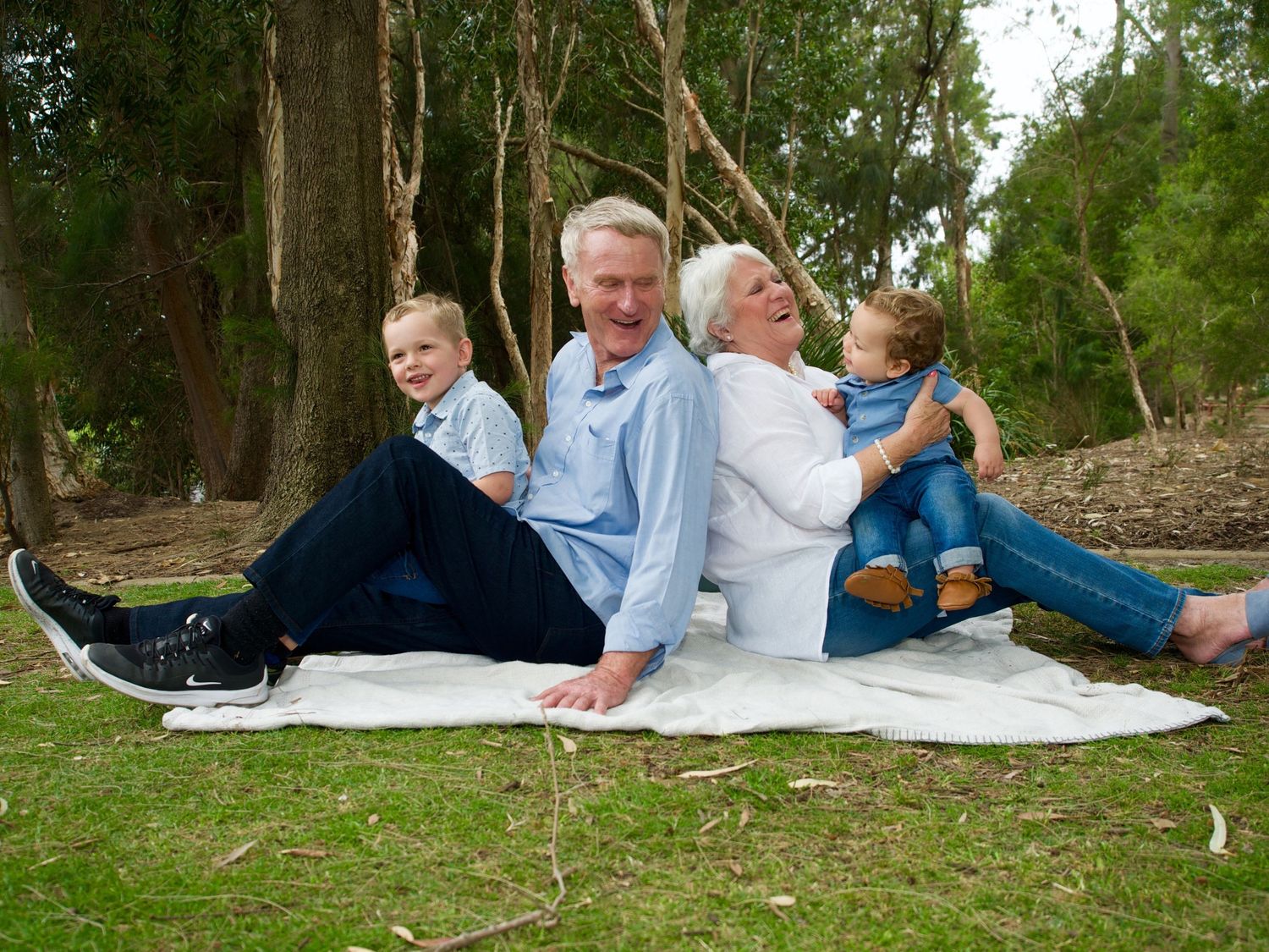 grandparents laughing and sitting on the ground at a park with grandchildren