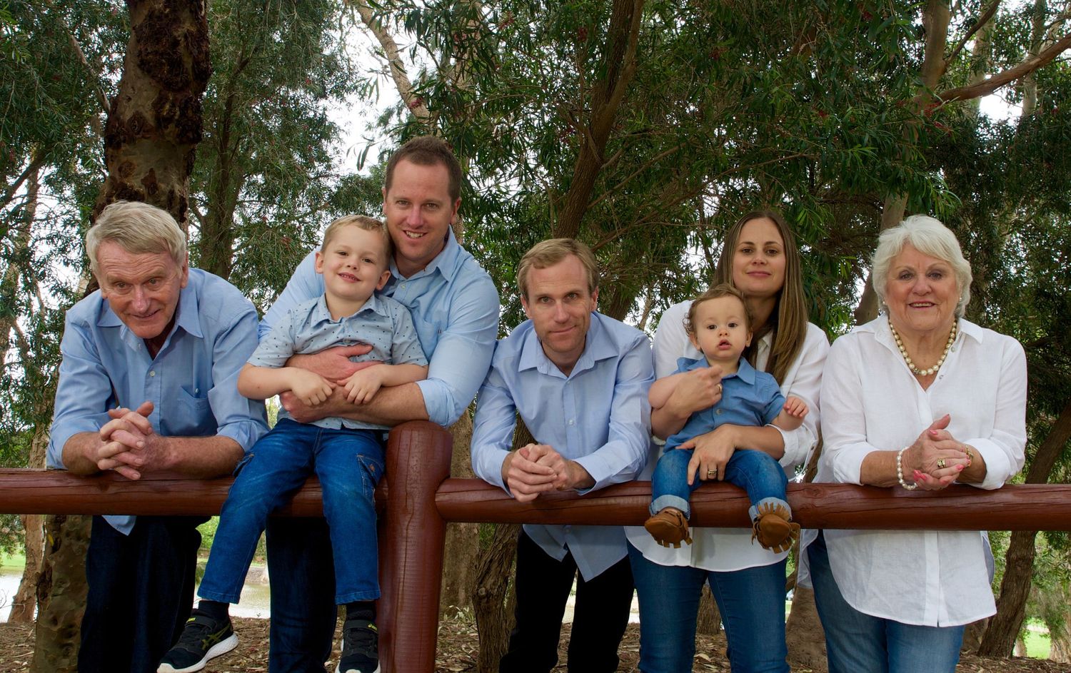 three generations family portrait leaning on a fence at a park