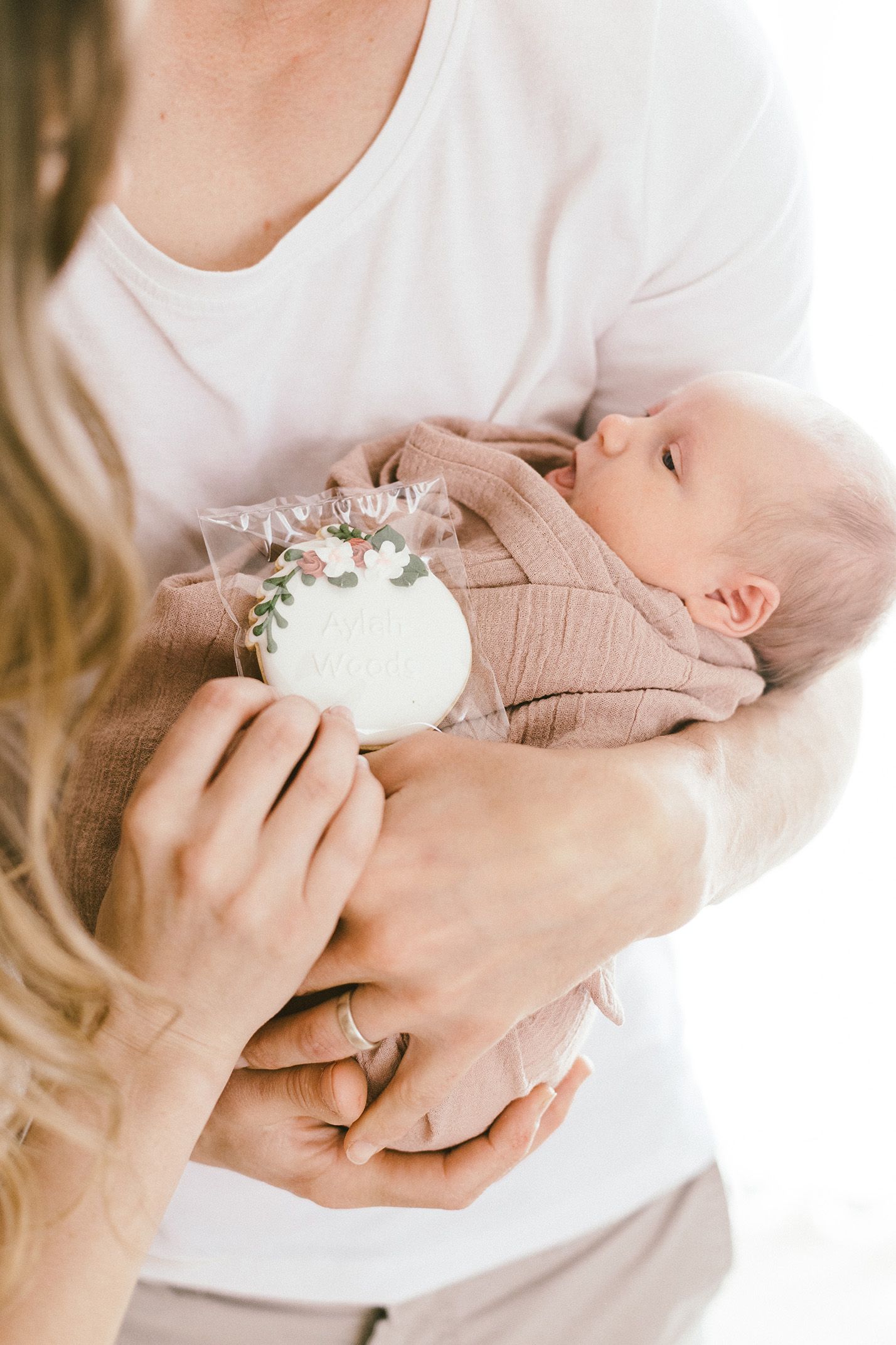 Parent in white shirt gently holding sleeping newborn wrapped in beige blanket.